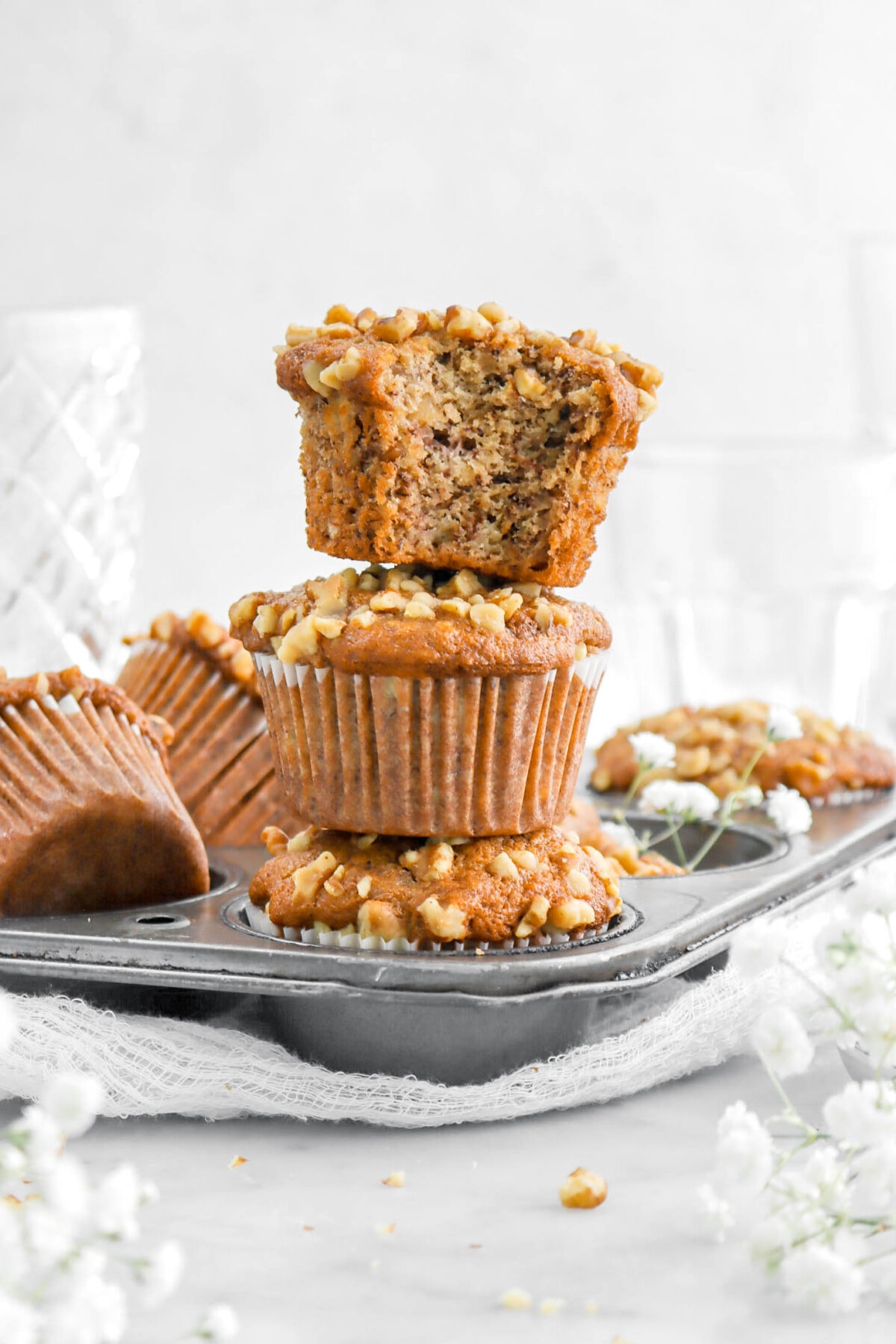 three stacked muffins with top muffin missing a bite in a muffin pan with more muffins behind.
