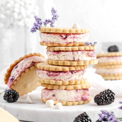 stacked ice cream sandwiches on marble plate with blackberries, white chocolate chips, and purple flowers around.