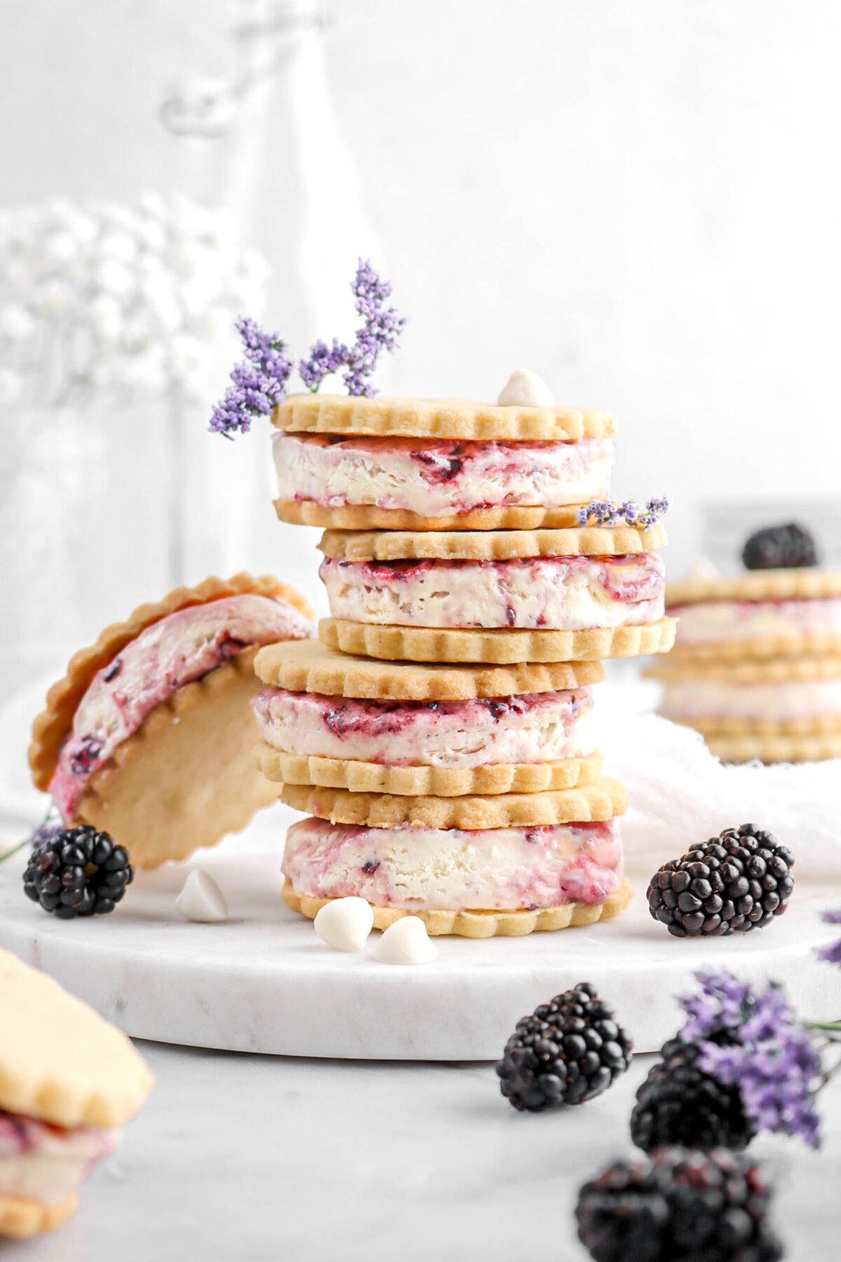 stacked ice cream sandwiches on marble plate with blackberries, white chocolate chips, and purple flowers around.