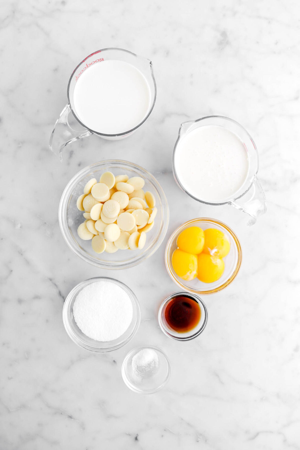 milk, cream white chocolate, egg yolks, sugar, vanilla, and salt on marble surface.