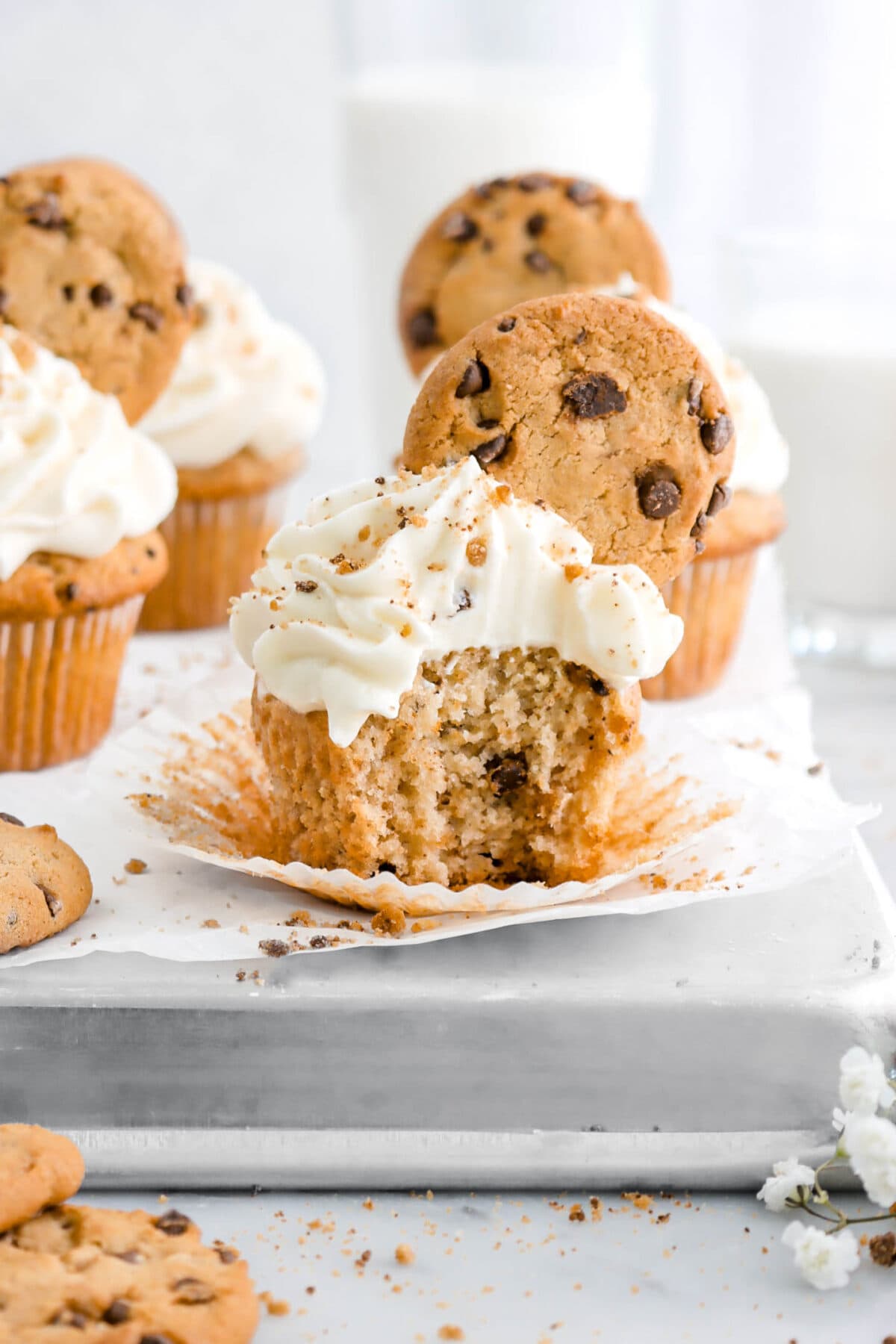 chocolate chip cookie cupcake with bite missing on cupcake paper on upside down sheet pan with more cupcakes behind.