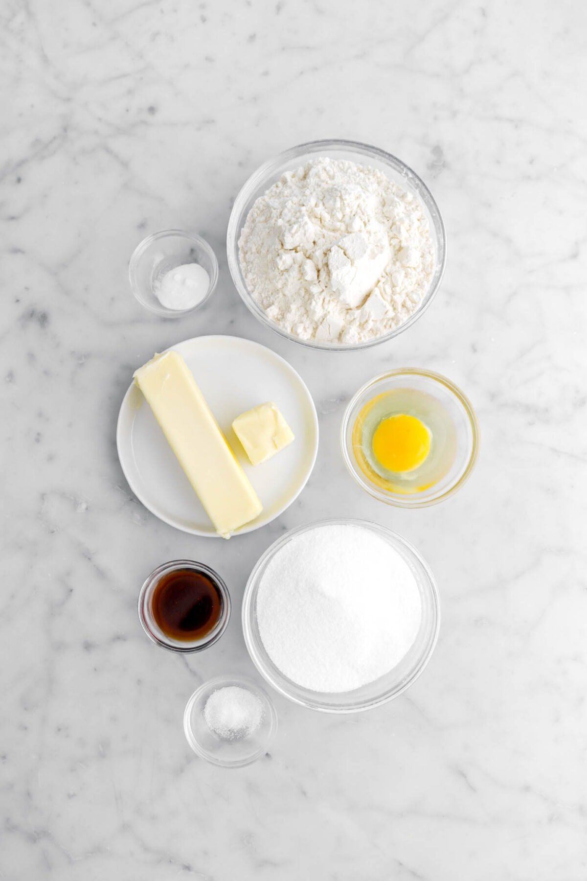 baking soda, flour, butter, egg, vanilla, sugar, and salt on marble surface.