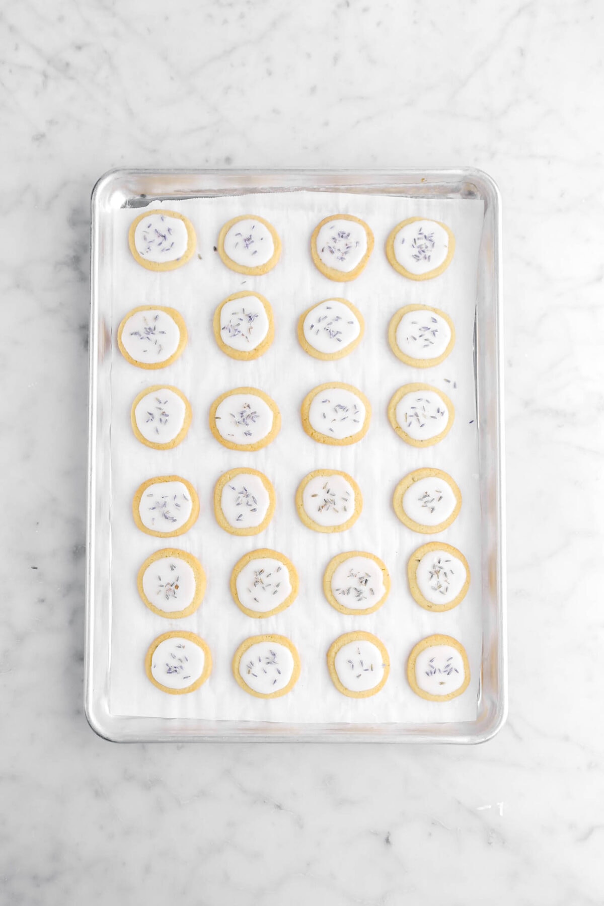 iced shortbread cookies with dried lavender on top on lined sheet pan.
