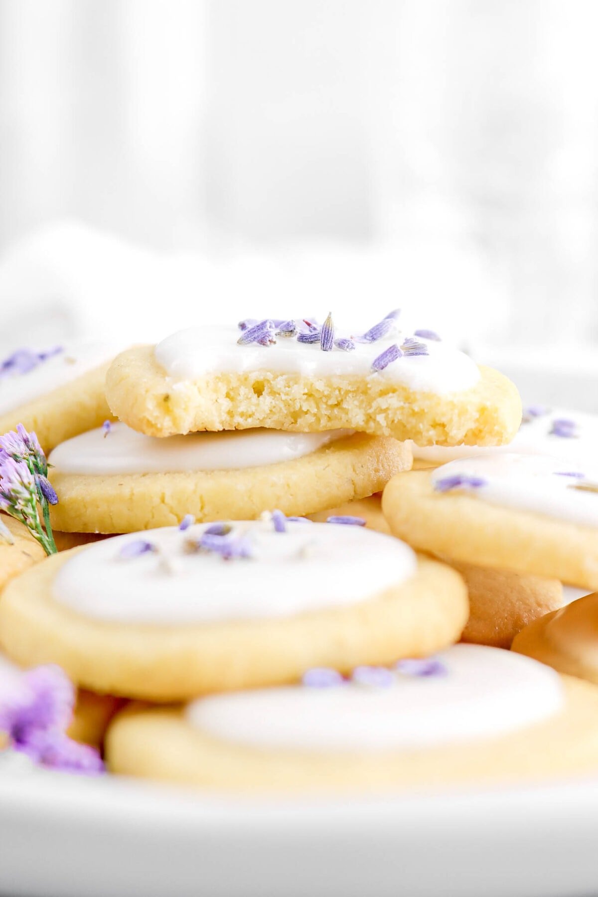 lavender cookie with bite missing facing forward on top of many other cookies.