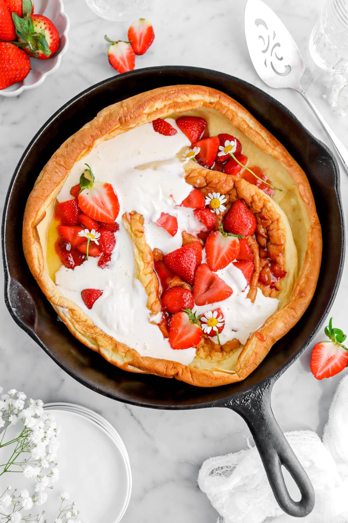 close up overhead shot of strawberries and cream dutch baby with chamomile flowers on top, with fresh strawberries around.