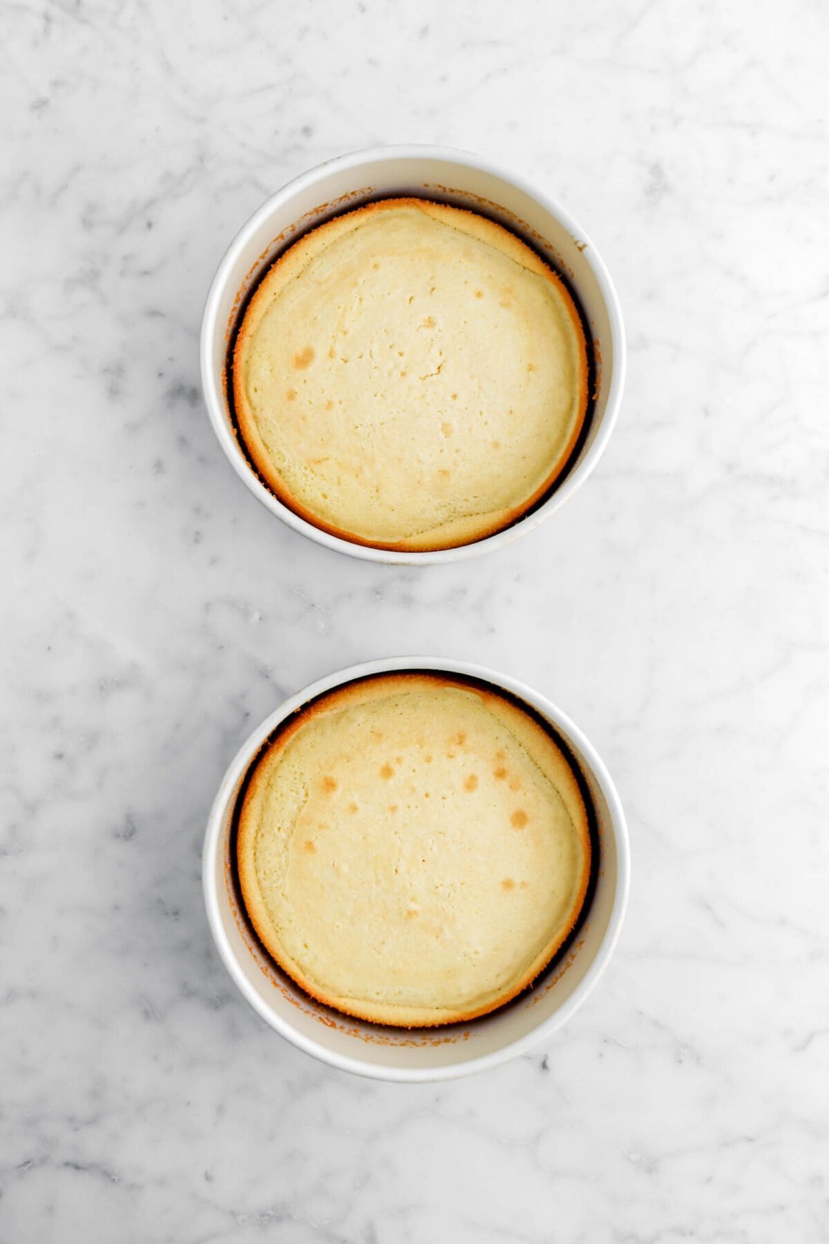 two baked vanilla cakes in round pans on marble surface.