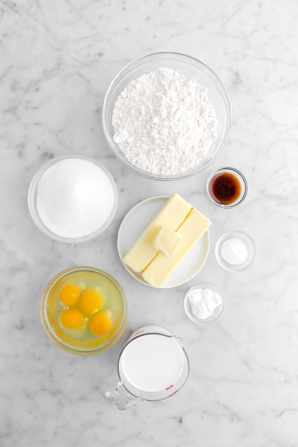 flour, sugar, vanilla, vanilla, salt, baking soda, eggs, and milk on marble surface.
