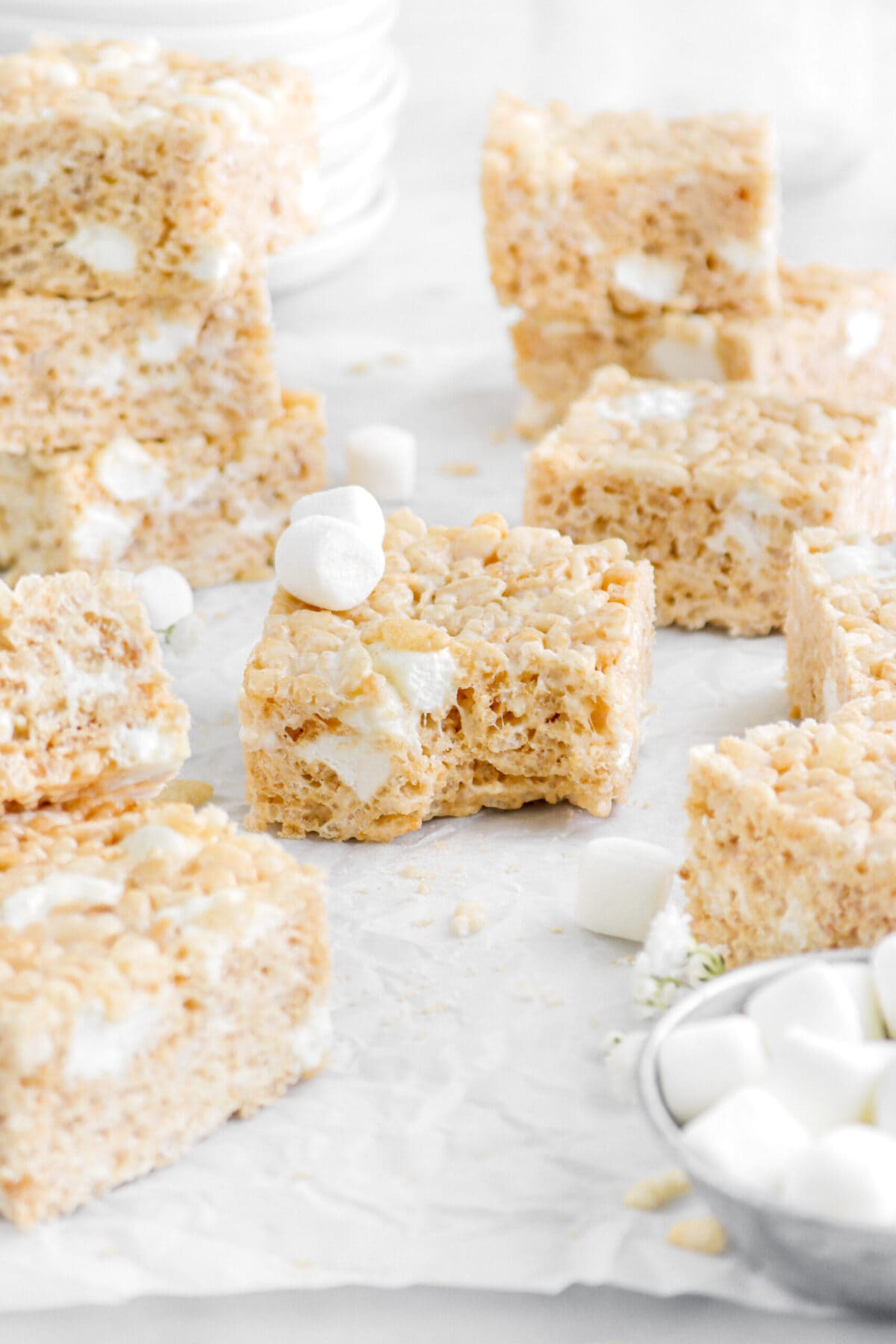 rice krispie treat with bite missing and two marshmallows on top with ten more rice krispie treats around.