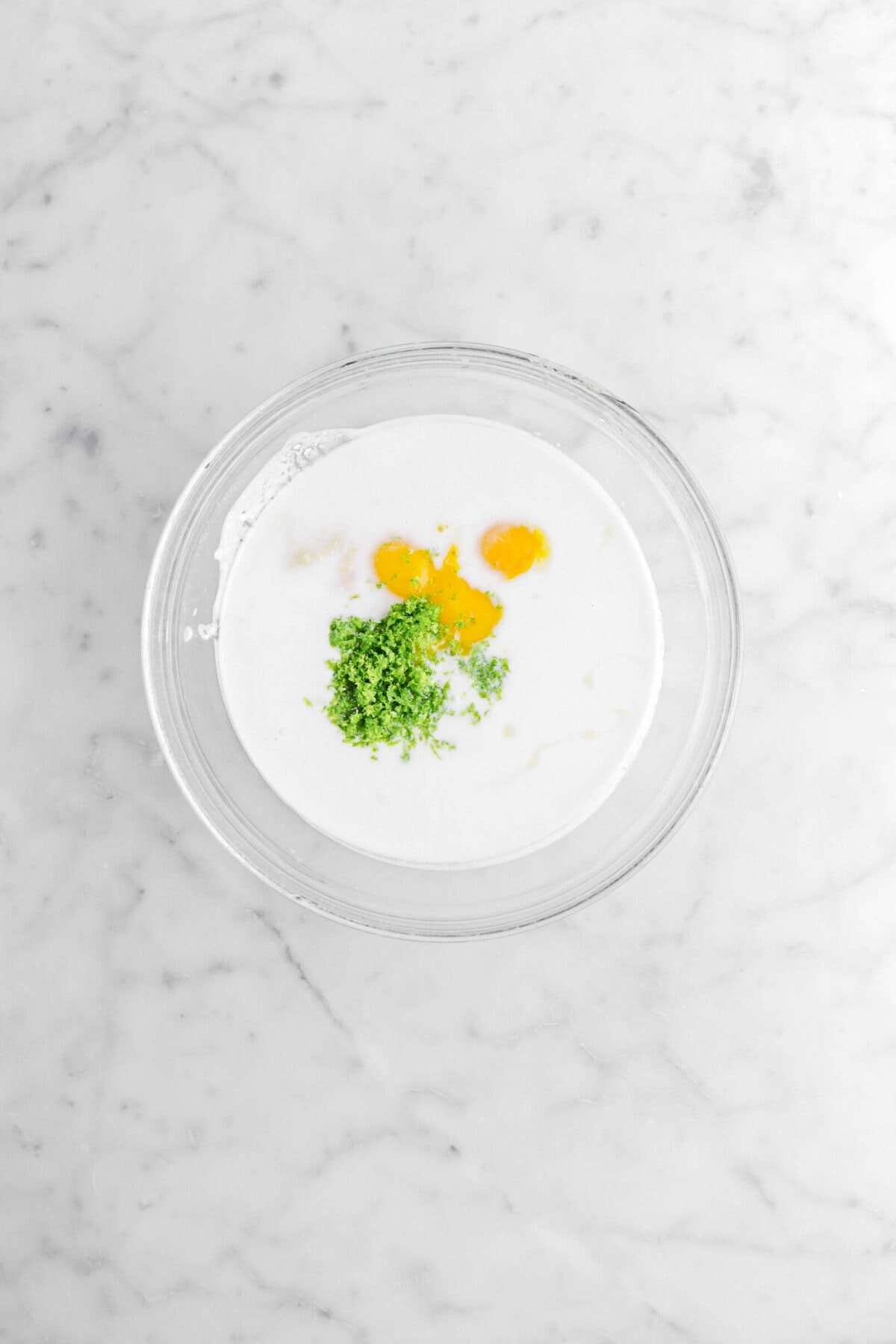milk, key lime zest, egg yolks, and grated ginger in glass bowl.