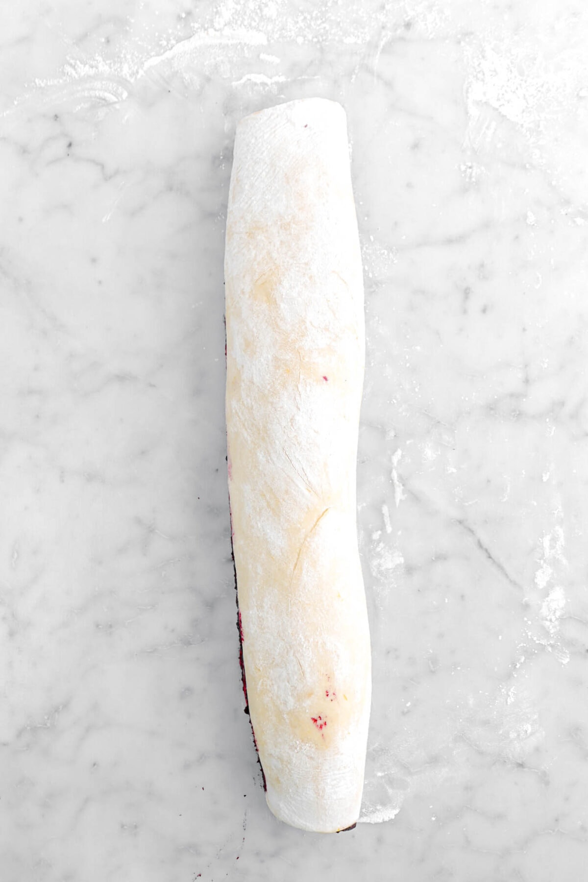 dough rolled into a log on marble surface.