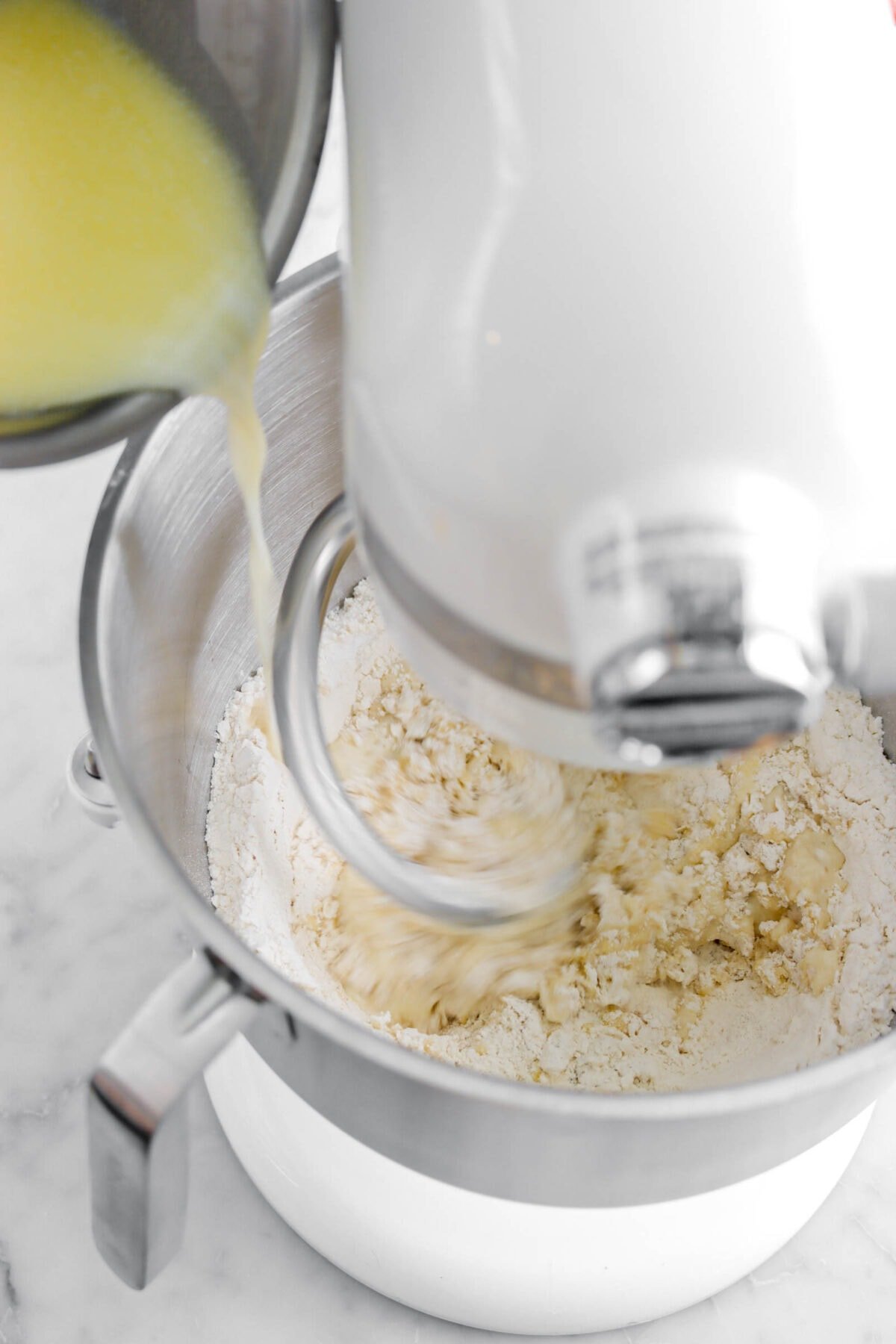 melted butter and milk mixture being poured into dry ingredients with mixer running.