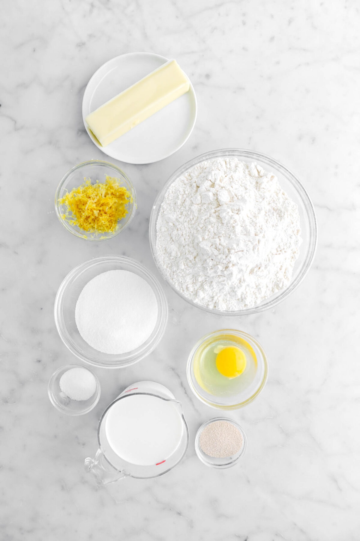 butter, lemon zest, flour, sugar, egg, salt, milk, and yeast on marble surface.
