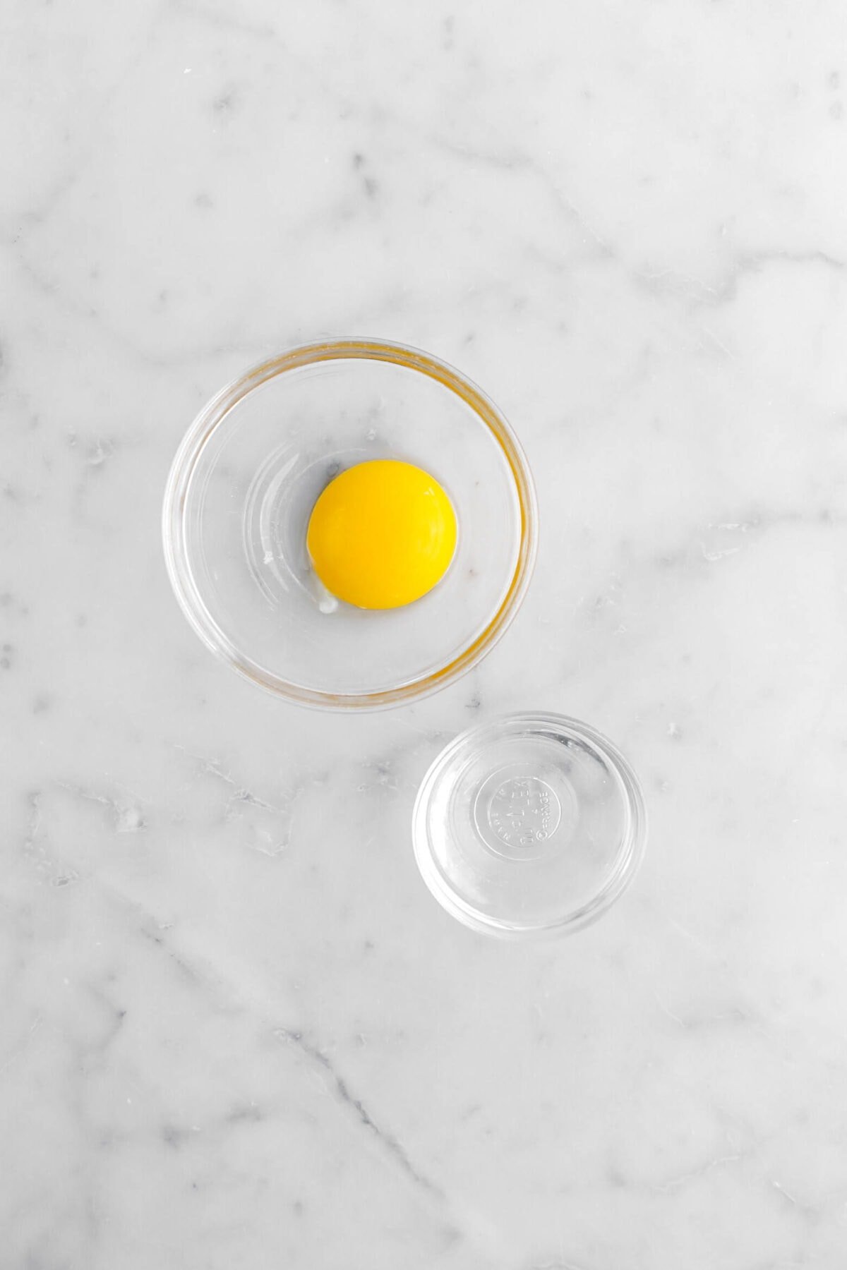 egg yolk and water in separate bowls on marble surface.