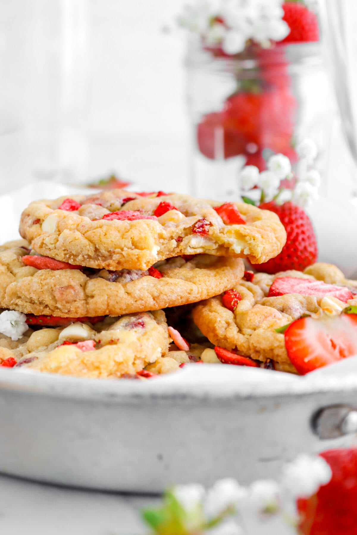 close up of stacked strawberry white chocolate cookies in pie plate with strawberries in jar behind.