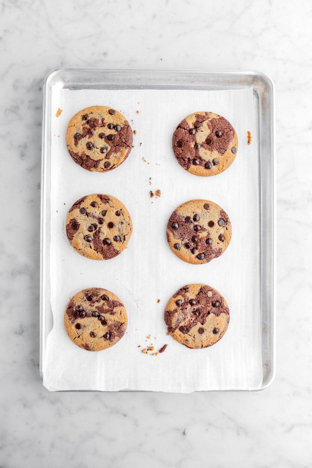 six baked chocolate peanut butter marble cookies on parchment lined sheet pan.