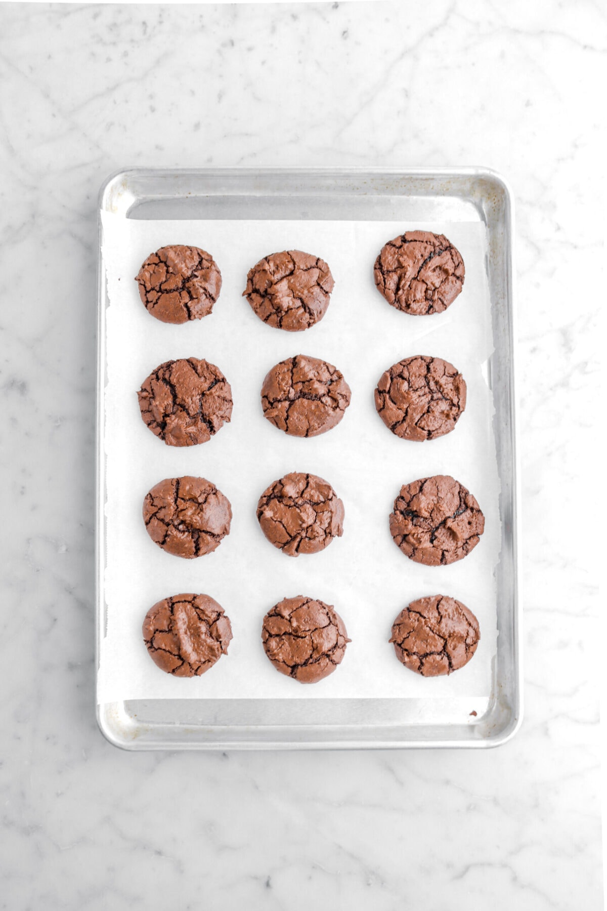 twelve baked brownie cookies on lined sheet pan.