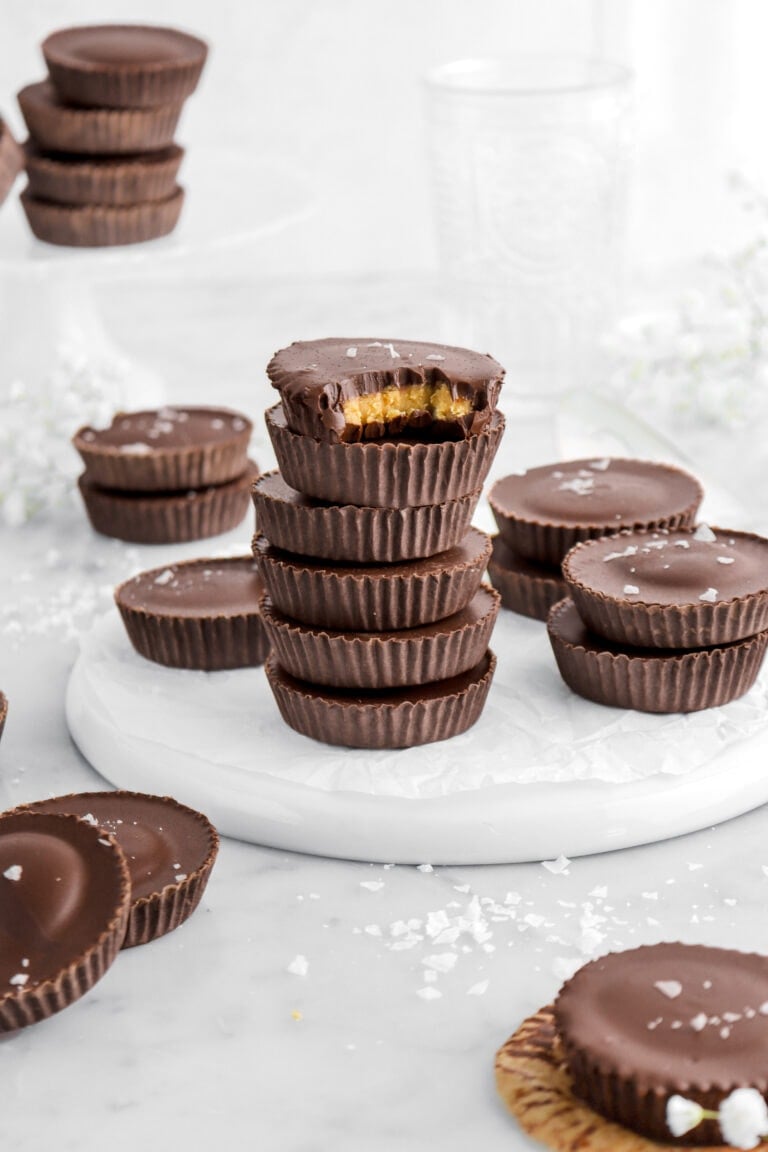 peanut butter cups stacked on upside down white plate with top candy missing a bite white flower and flaked salt around.