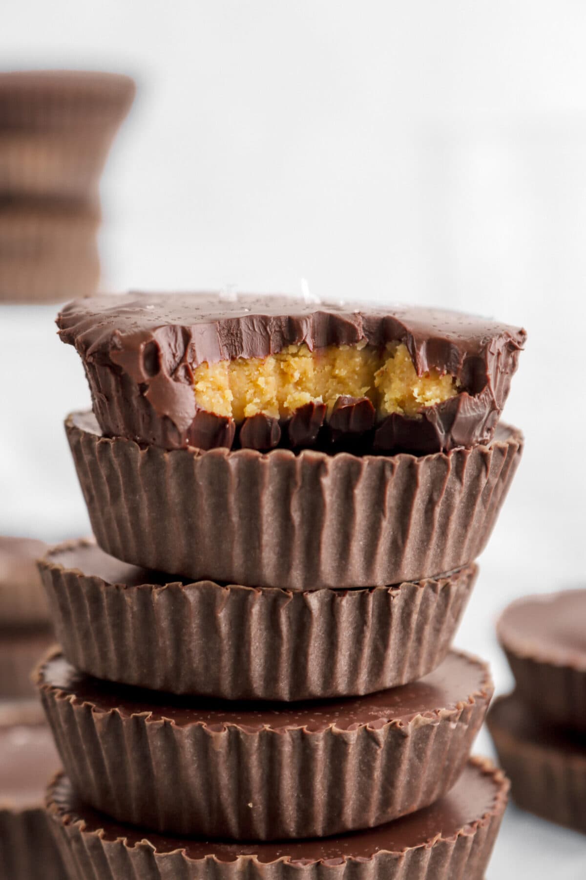 cropped close up of peanut butter cup with bite missing stacked on top of four more candies.