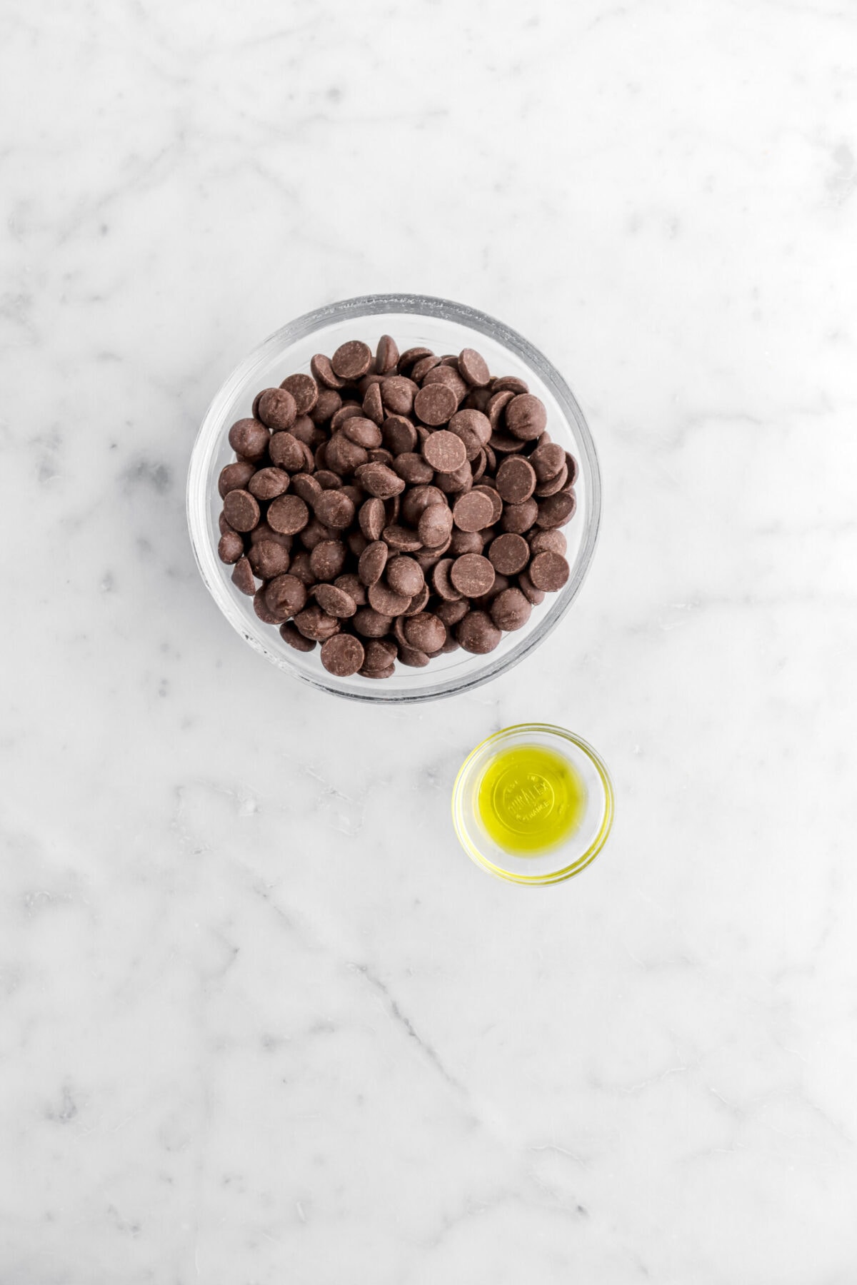 chocolate chips and olive oil in separate glass bowls on marble surface.