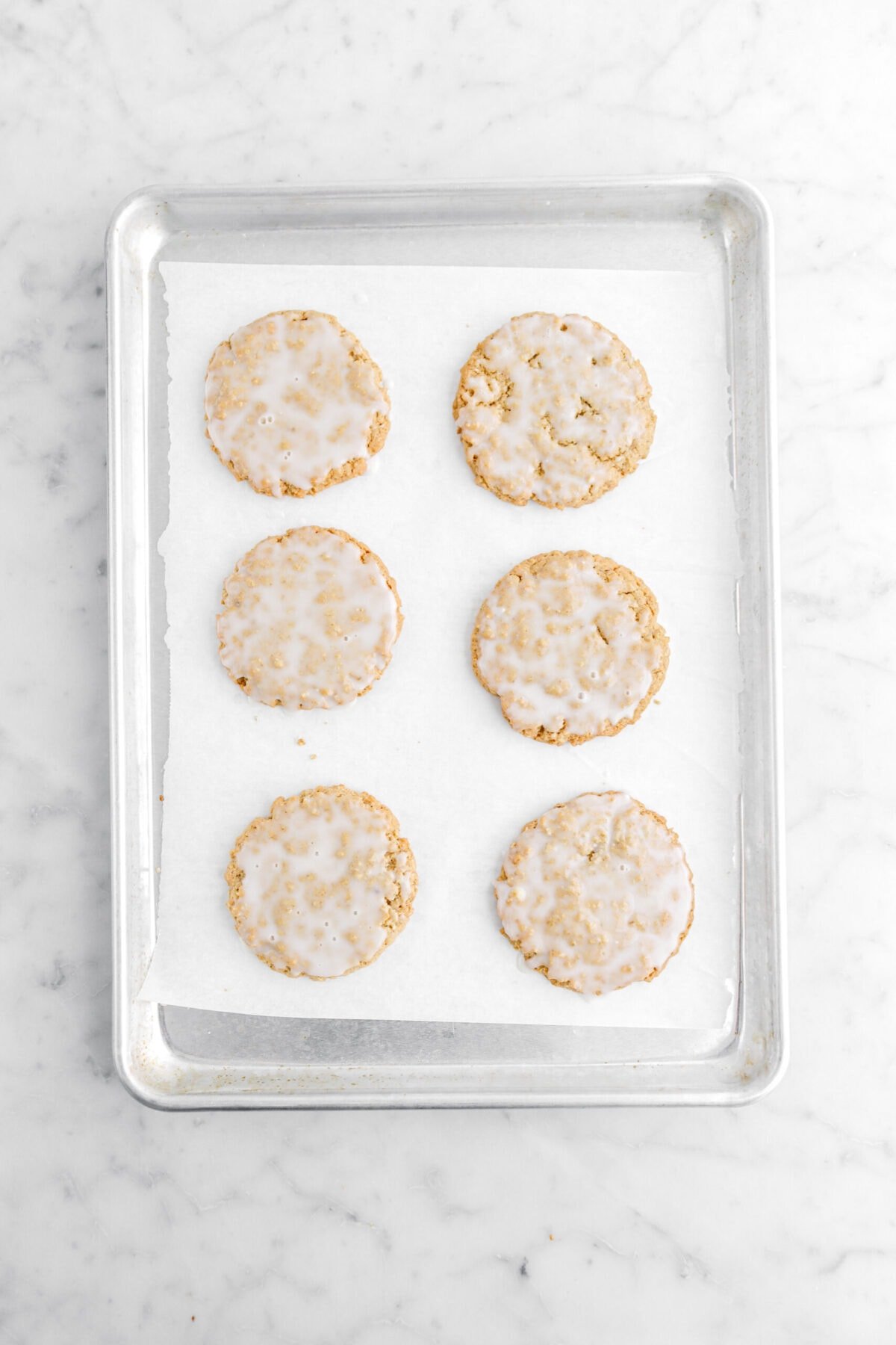 six iced oatmeal cookies on lined sheet pan.