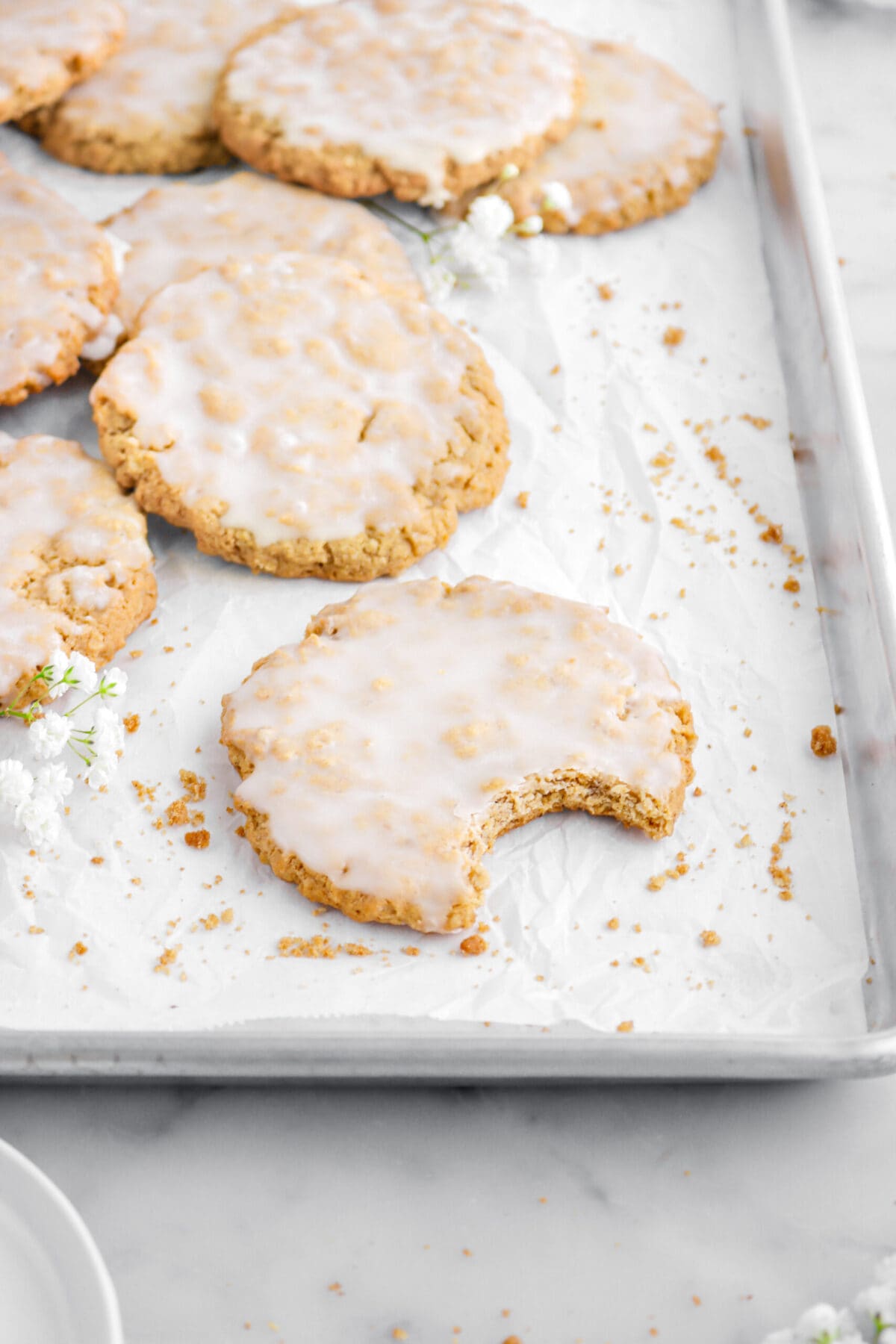 angled shot of iced oatmeal cookie with bite missing on lined sheet pan with more cookies behind.