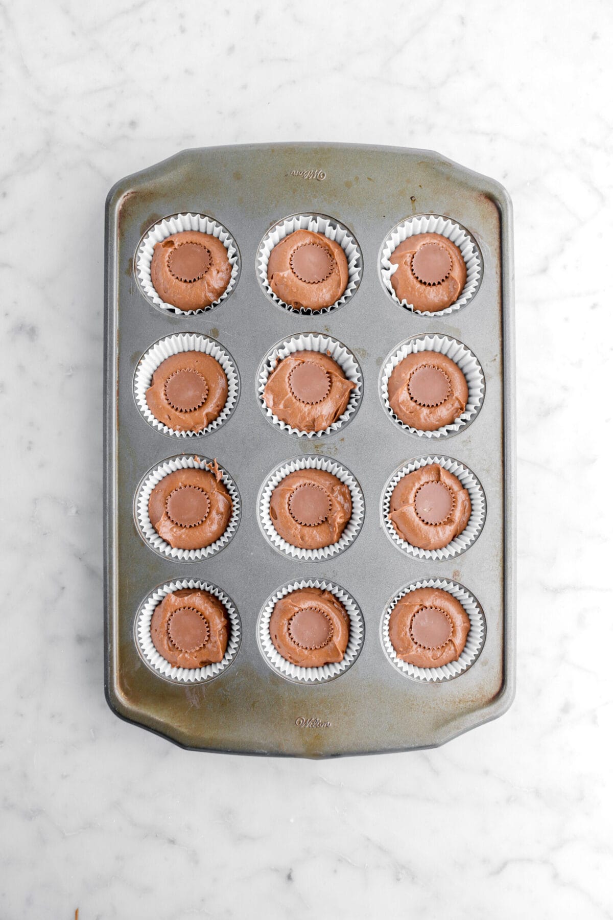 cupcake batter in muffin pan with mini peanut butter cup in the middle of each.