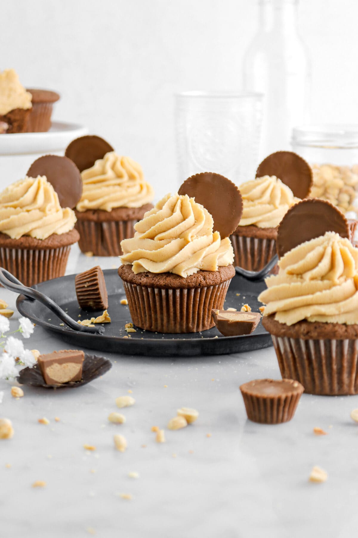 front shot of five chocolate cupcakes with peanut butter frosting on marble surface with peanut butter cups and peanuts scattered around.