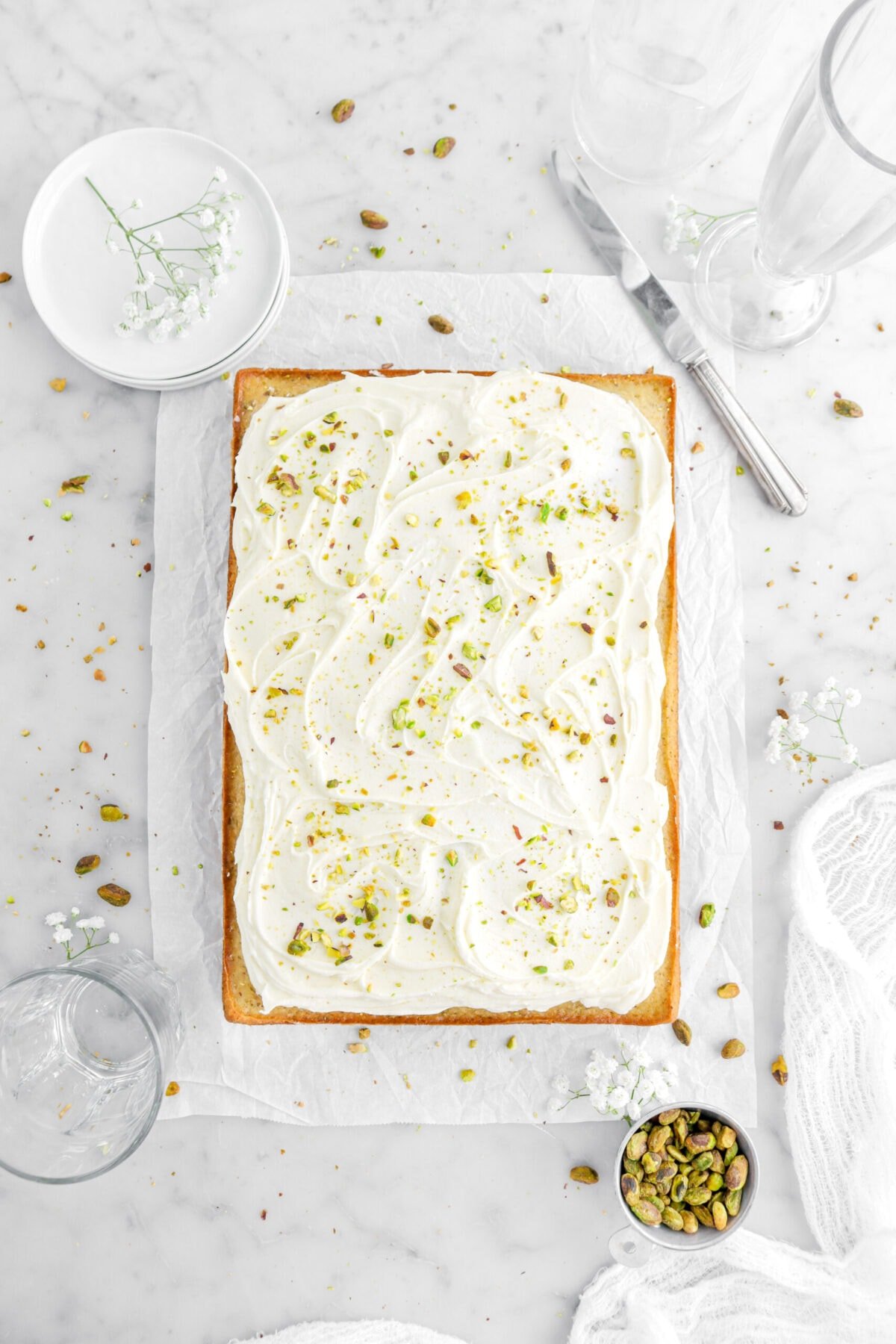 pistachio sheet cake on parchment paper with buttercream frosting and pistachios around with white flowers.