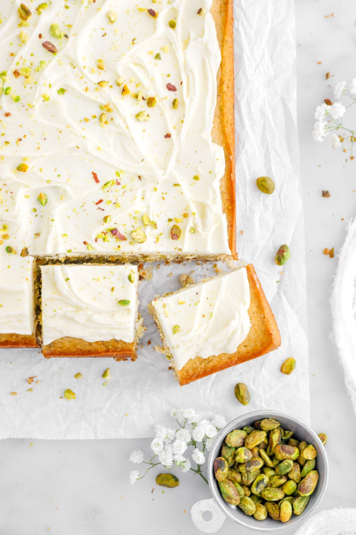 cropped overhead shot of pistachio cake with two slices cut into it and bowl of pistachios beside.
