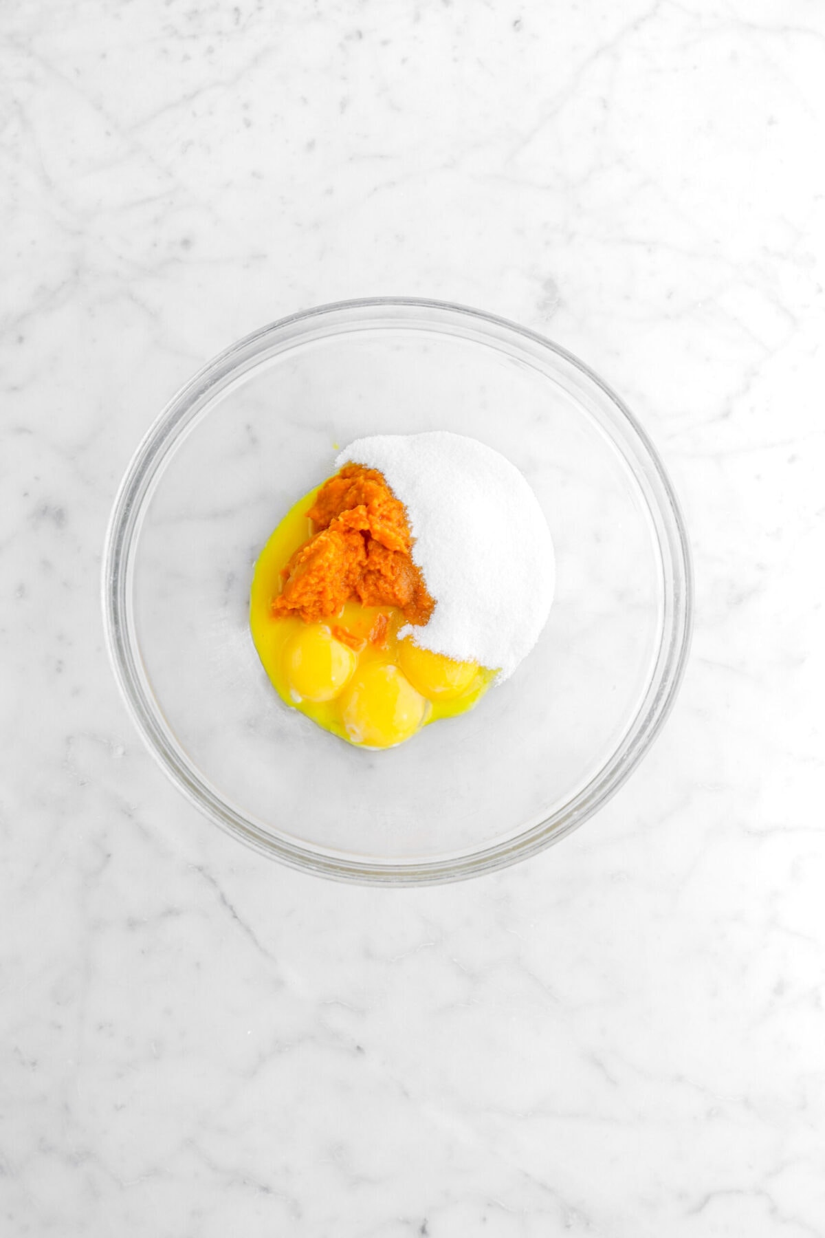 sugar, pumpkin puree, and egg yolks in glass bowl.