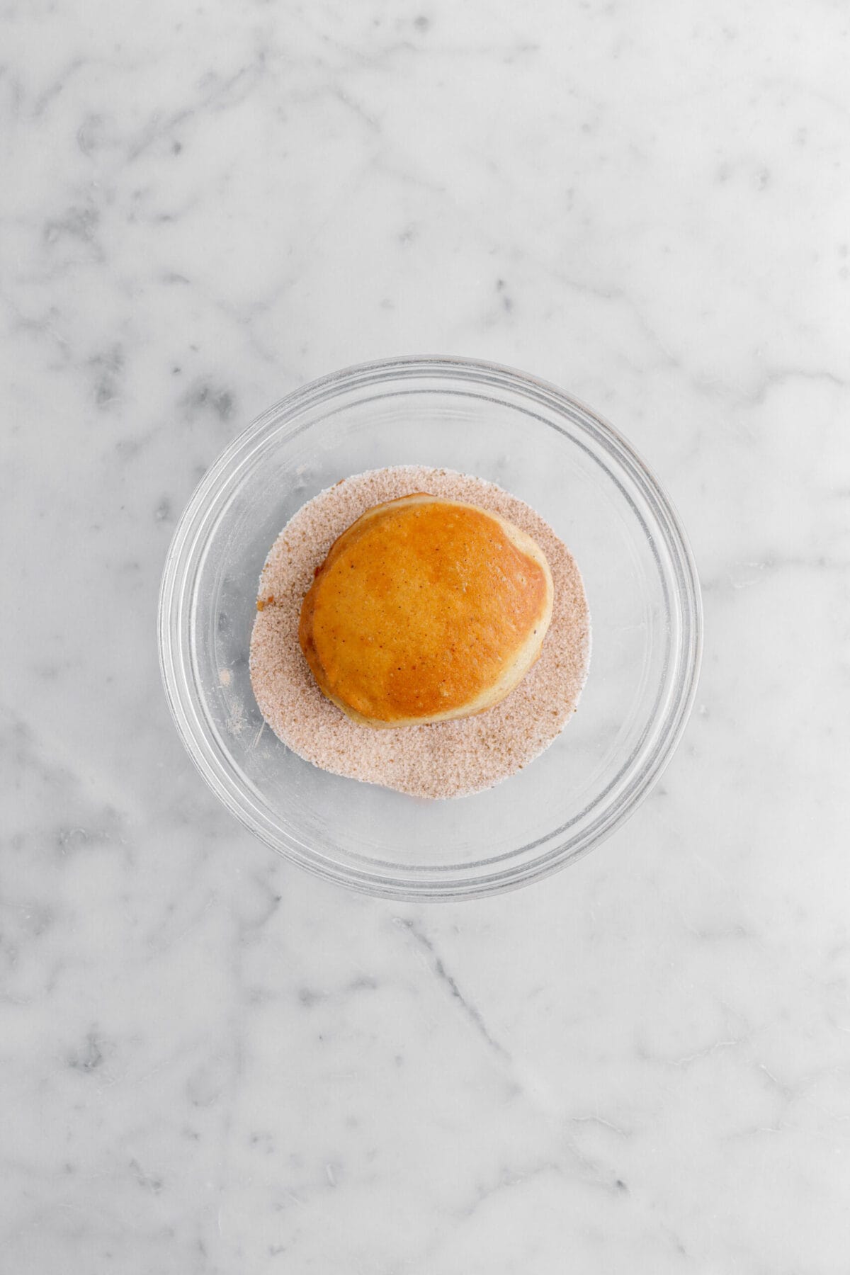 doughnut in spiced sugar mixture in glass bowl.
