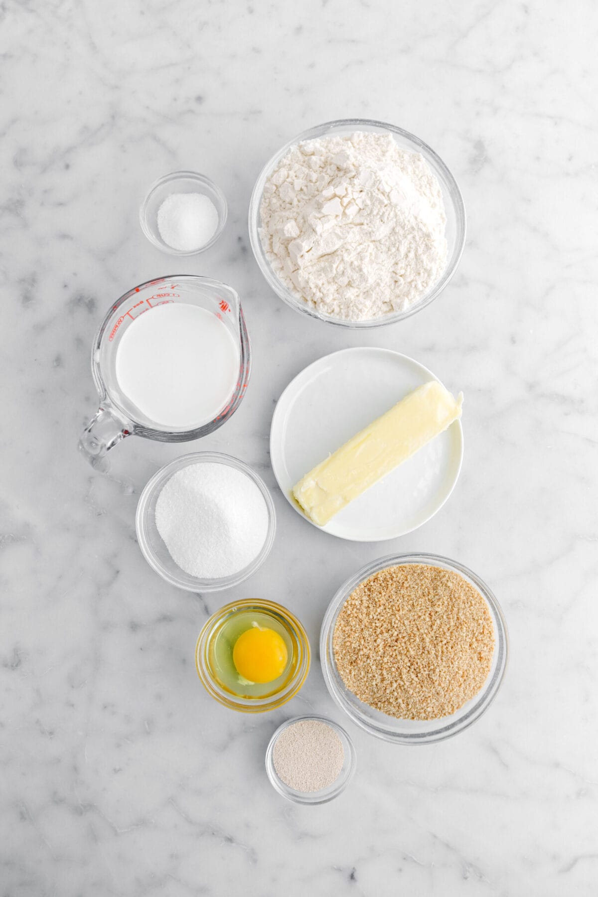 salt, flour, milk, butter, sugar, egg, graham cracker crumbs, and yeast on marble surface.