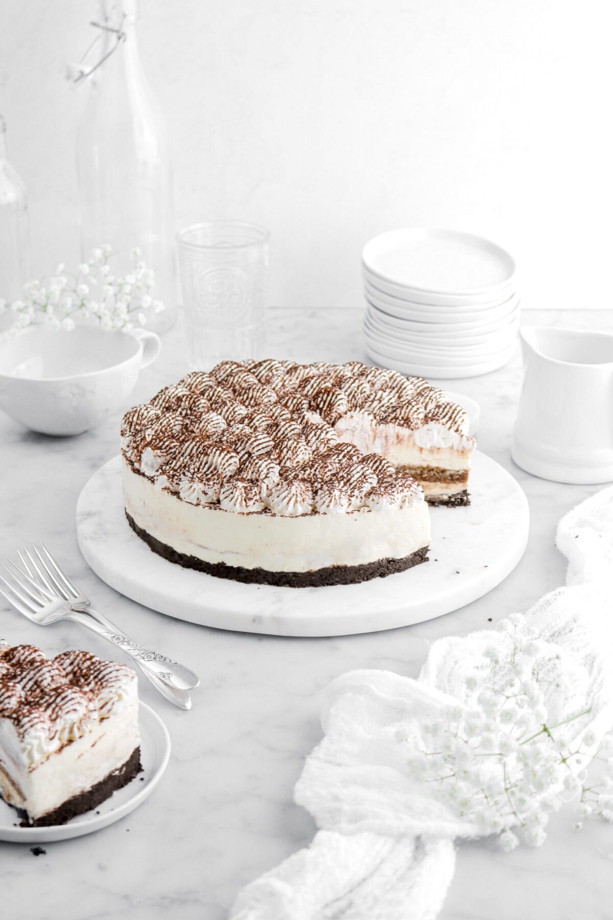 tiramisu cheesecake on round marble serving tray with slice on small white plate with two forks beisde.