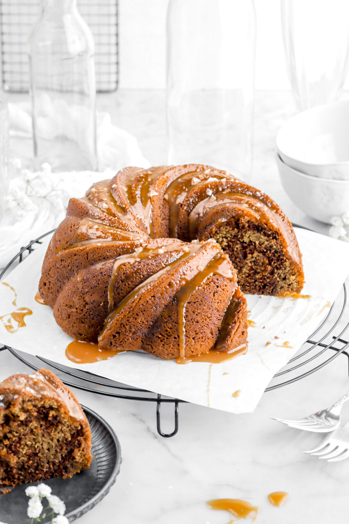 cut bundt cake on wire cooling rack with caramel sauce and salt flakes on top with slice of cake on plate beside.