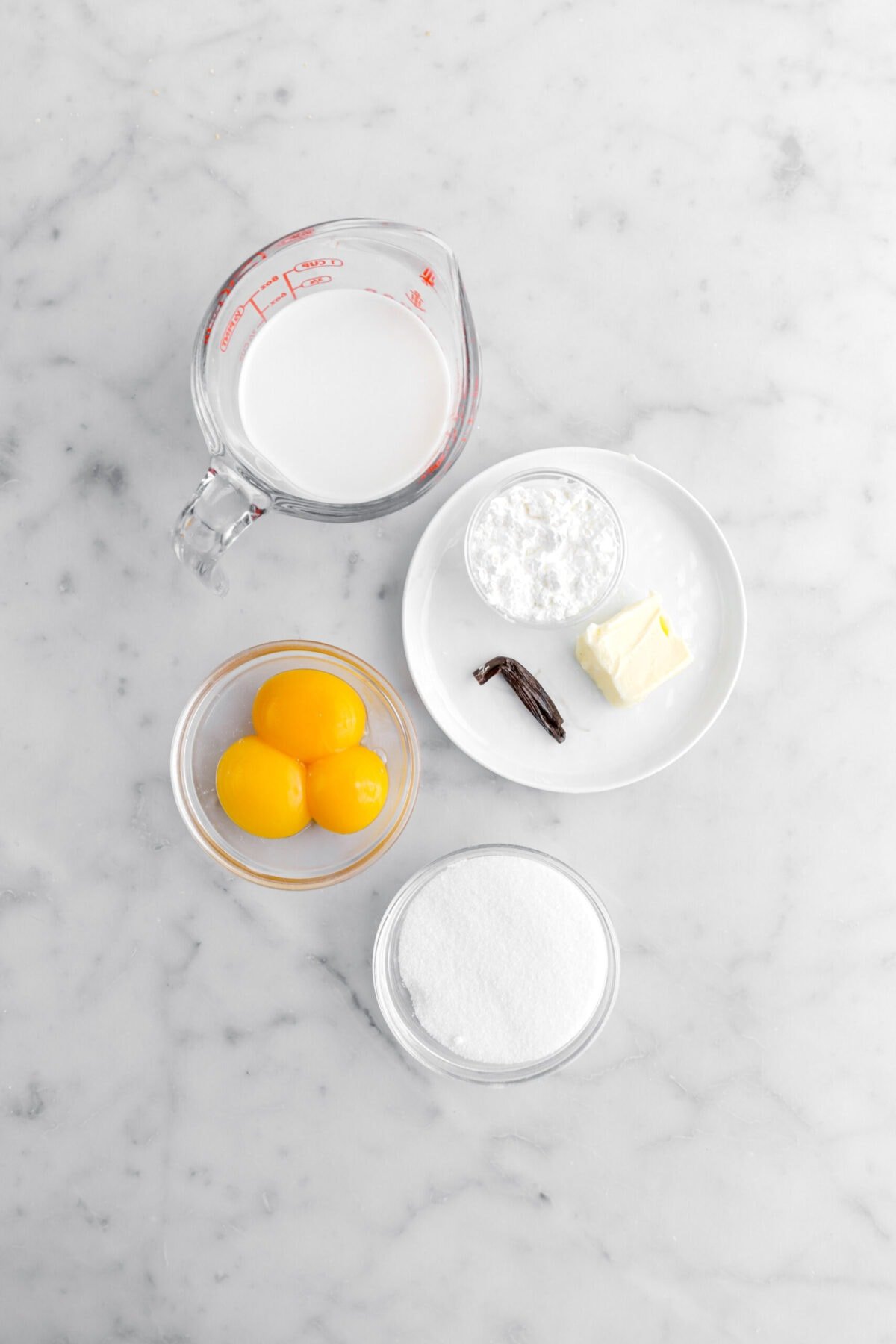 milk, corn starch, butter, vanilla bean, eggs, and sugar on marble surface.