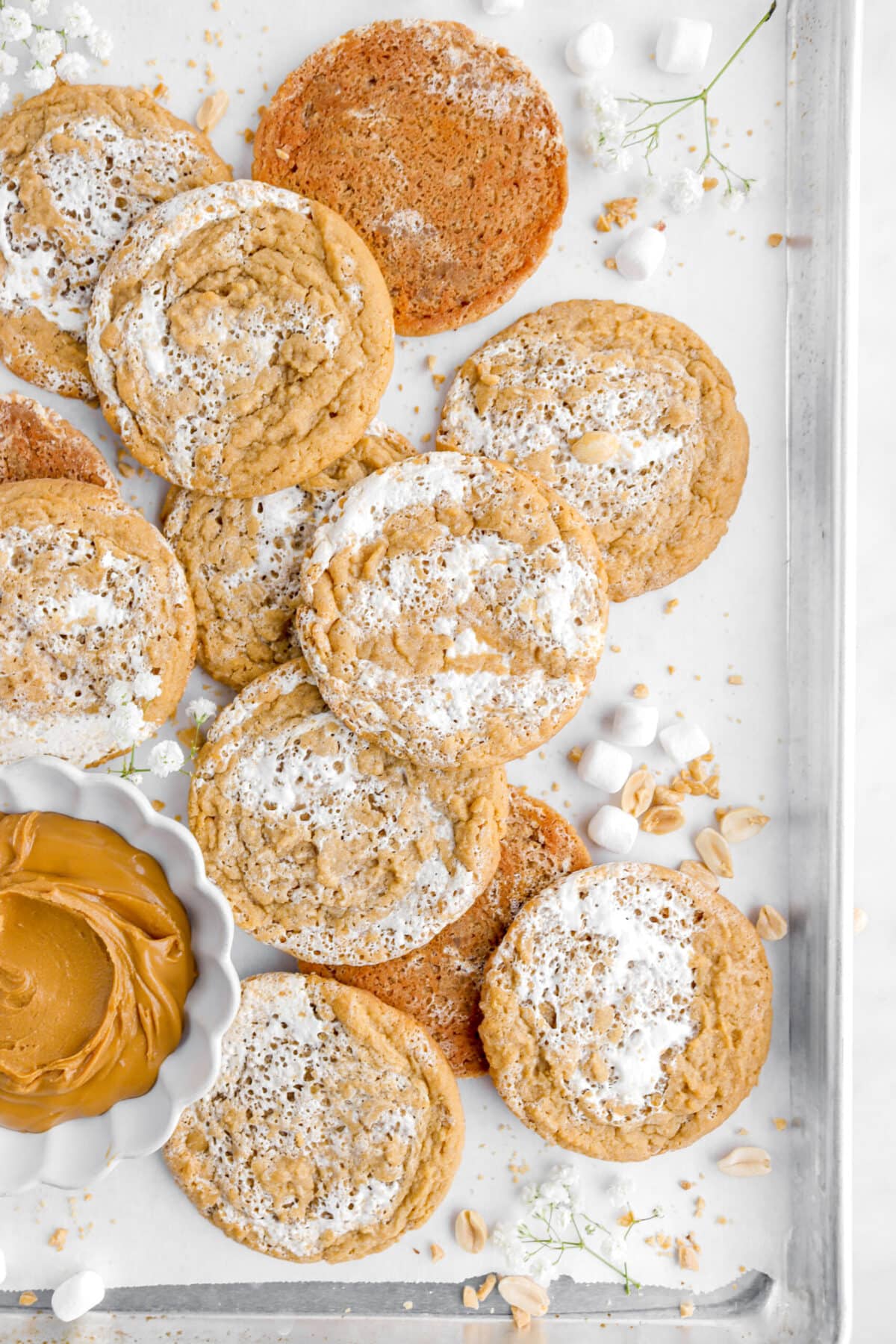 cropped overhead image of peanut butter marshmallow cookies on parchment lined sheet pan with bowl of peanut butter and mini marshmallows around.