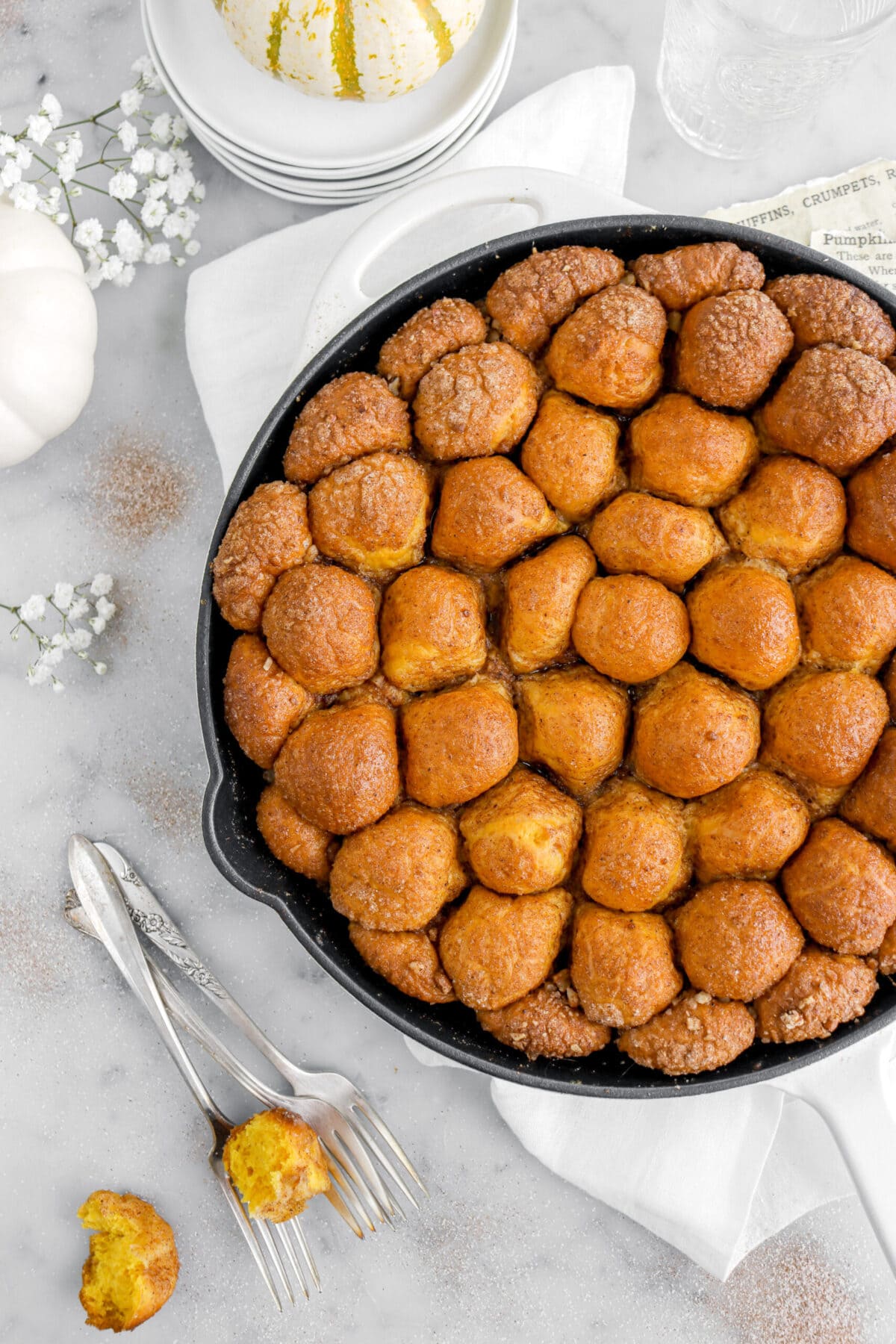cropped overhead image of pumpkin monkey bread in skillet with three forks beside and white flowers around.