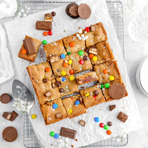 overhead image of cookie bars on wire cooling rack with one cookie turned on its side with candy around.