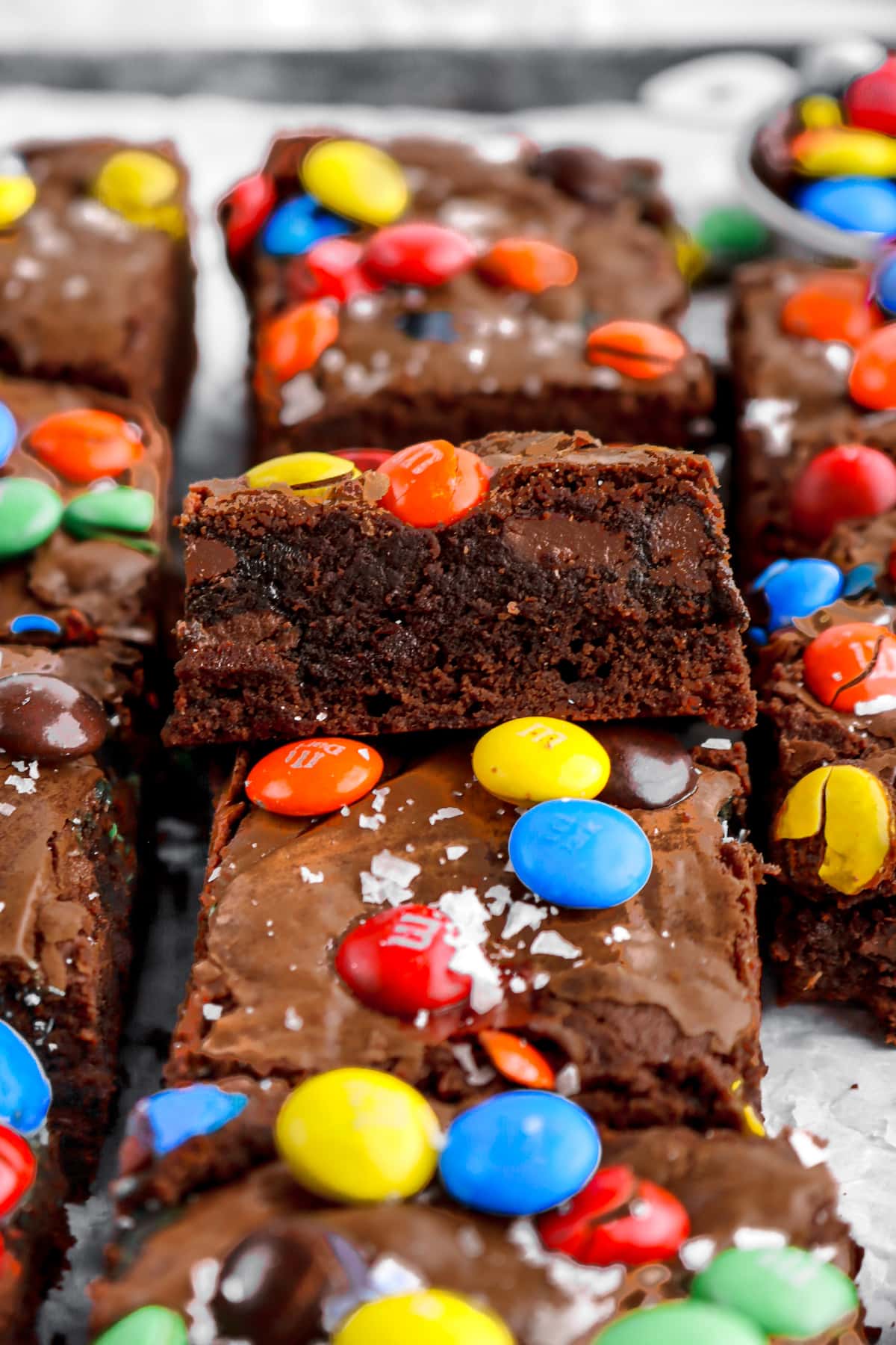 M&M brownie propped against another brownie with more around on lined sheet pan.