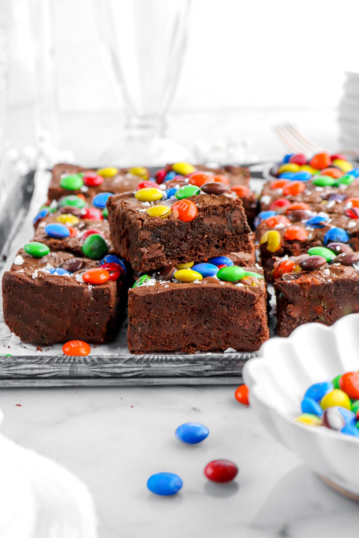 M&M brownies on lined sheet pan with one brownie on top of two more brownies.