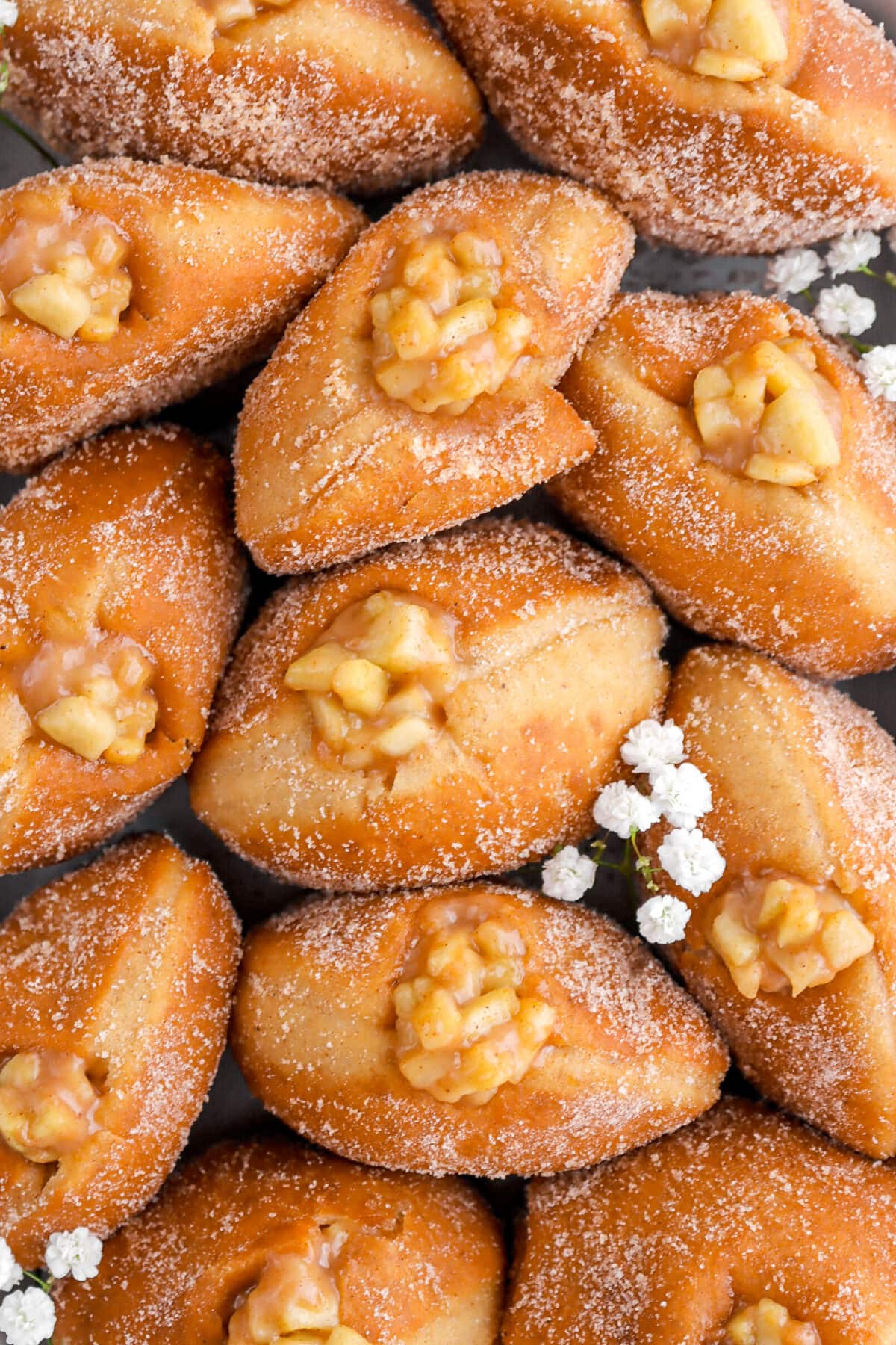 overhead close up of apple pie doughnuts all standing vertically with white flowers around.
