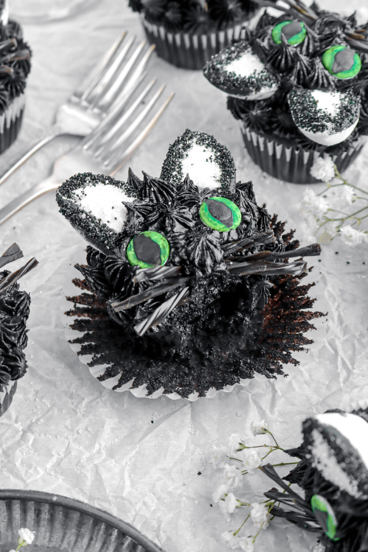 angled image of black cat cupcake with bite missing and more cupcakes behind.
