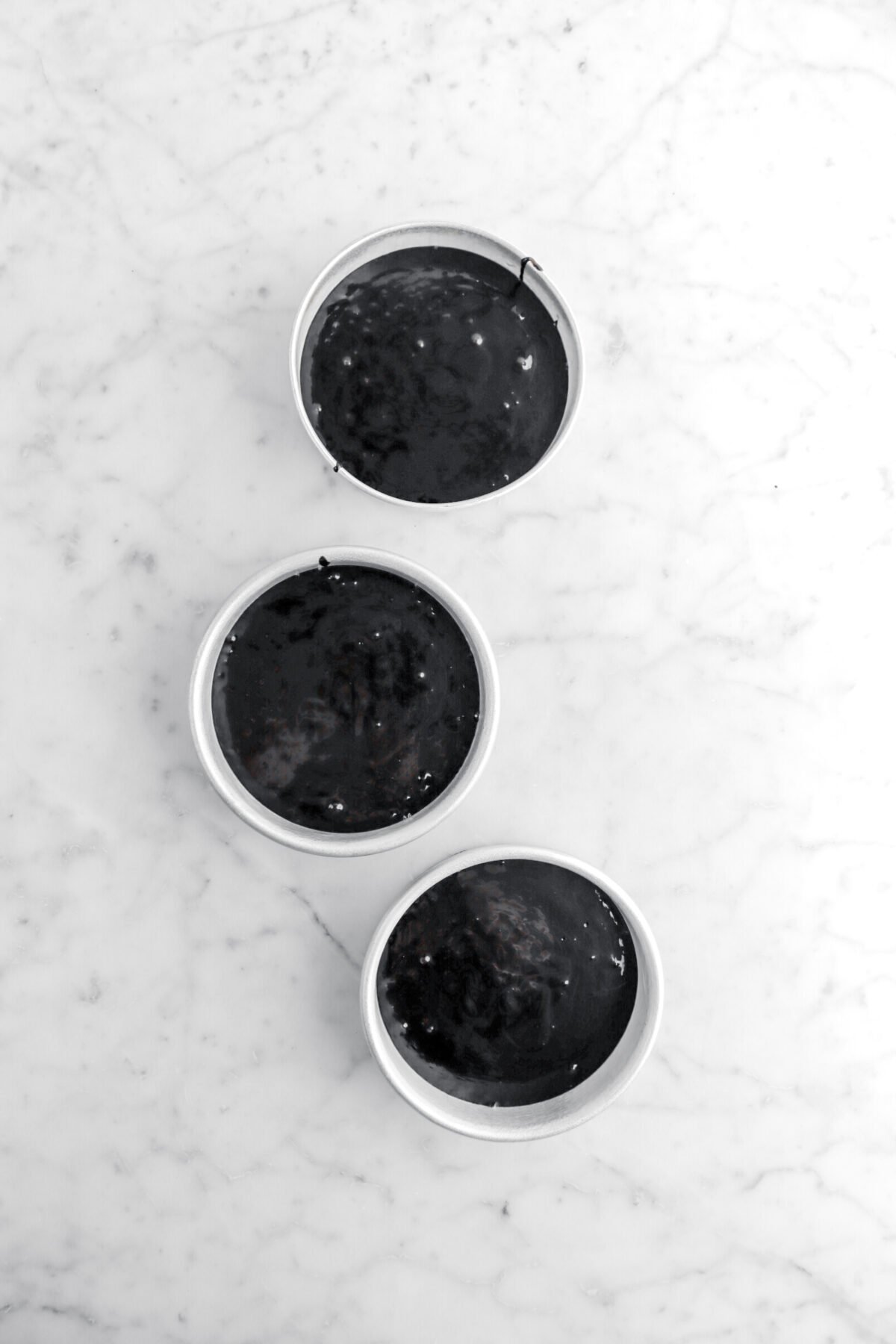 black cake batter in three small cake pans.