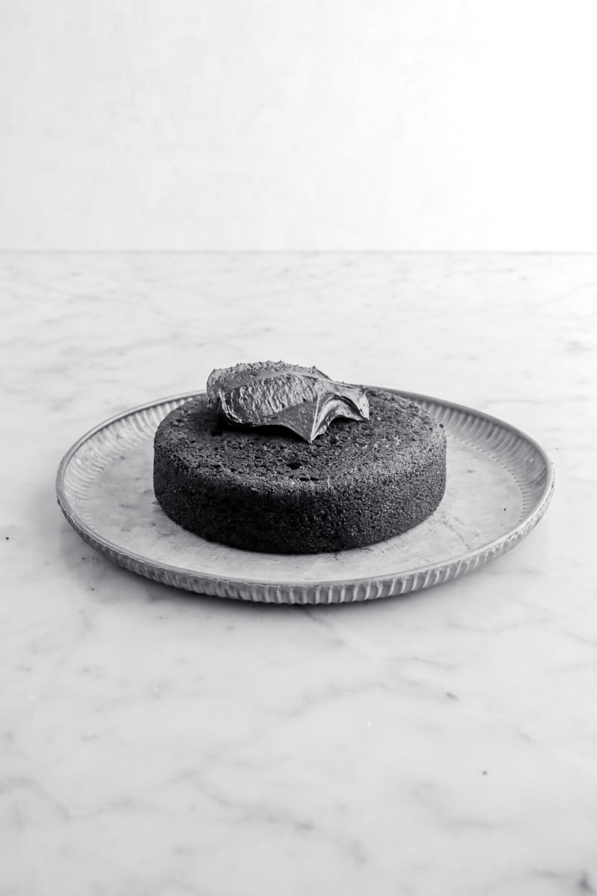 cake layer with black frosting on top of metal plate on marble surface.