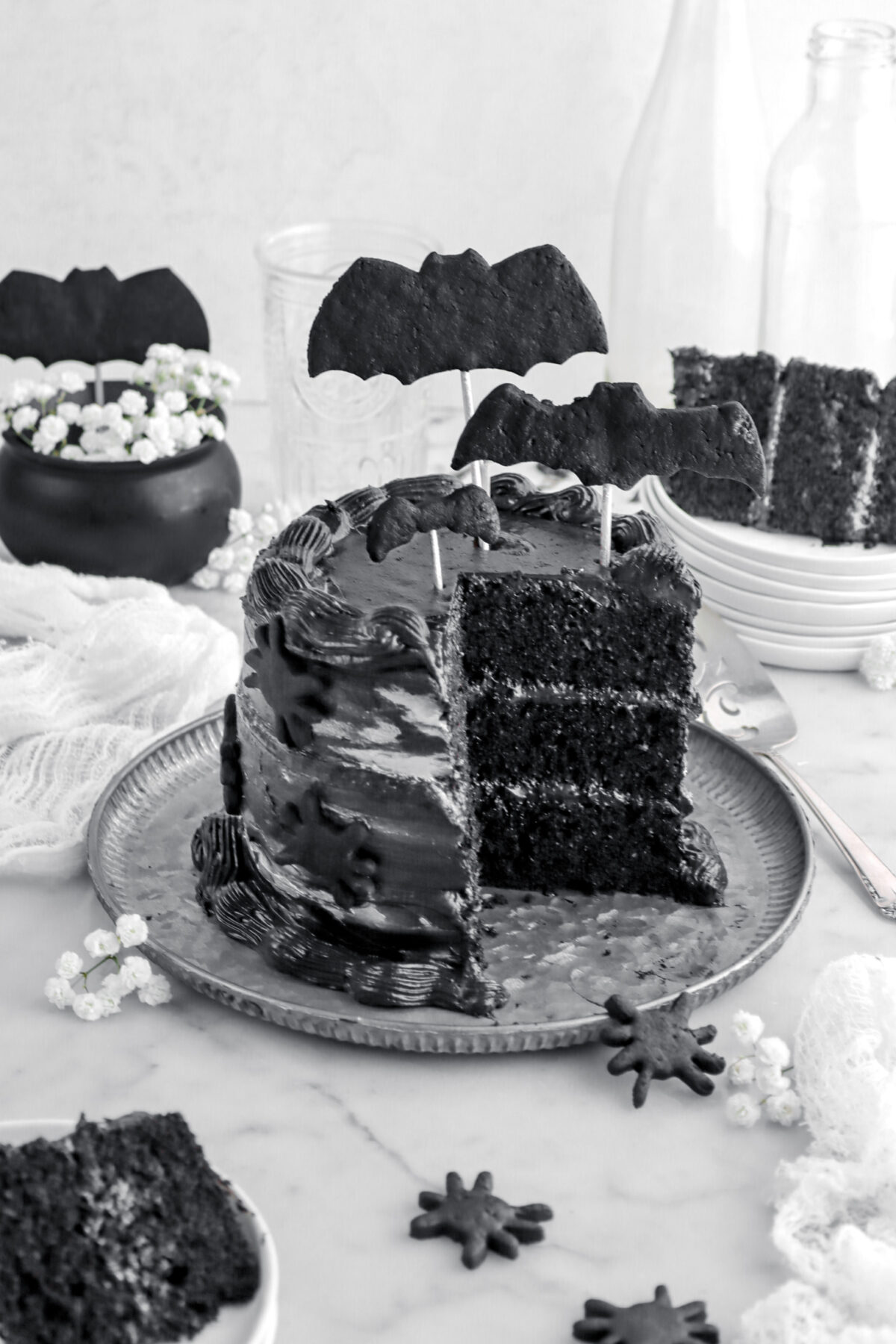 angled image of slices black velvet cake on metal plate with black bats on top and spiders on the side with two slices of cake around.