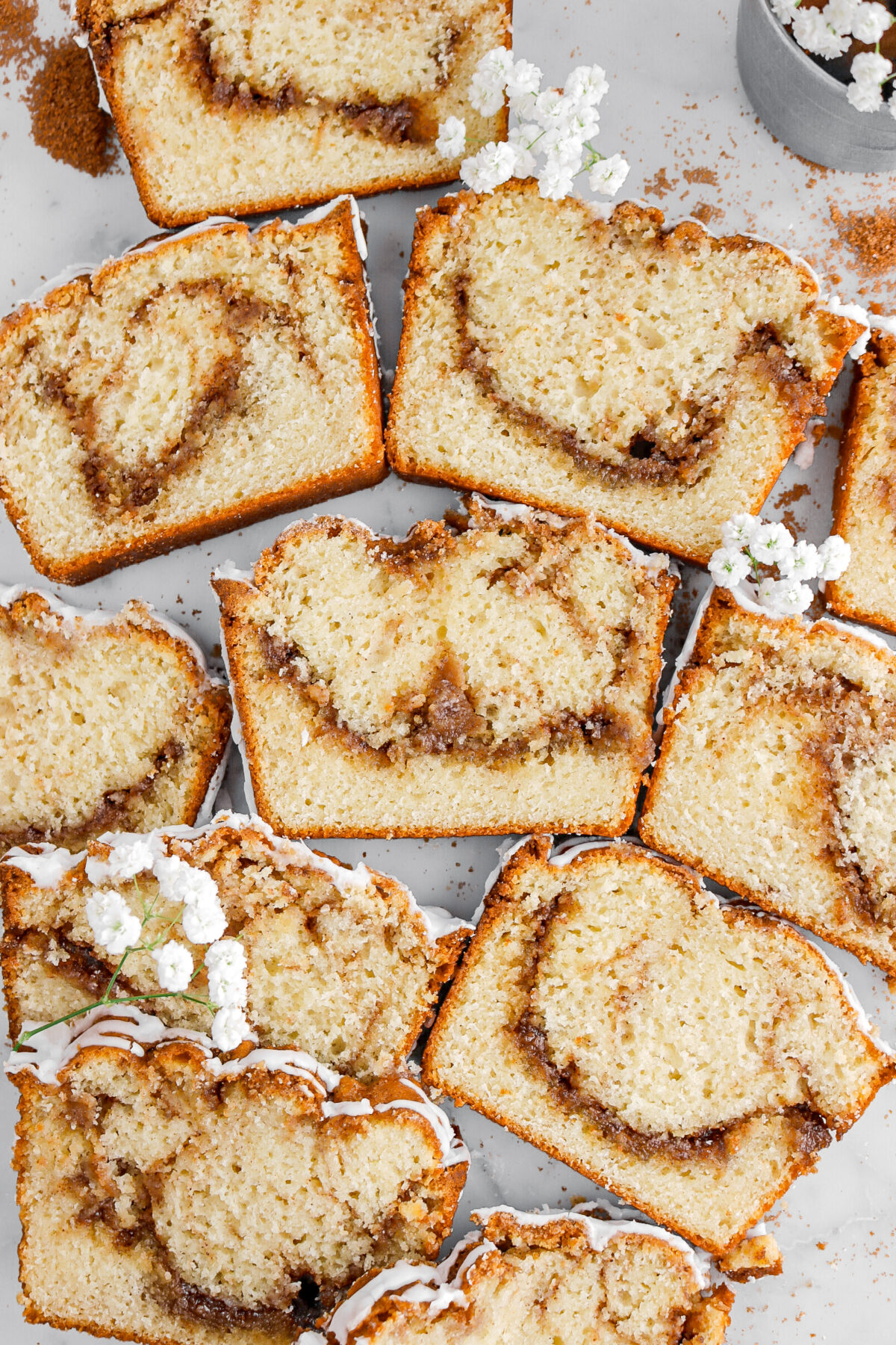 overhead image of eleven slices of cinnamon swirl bread on marble surface with white flowers around.
