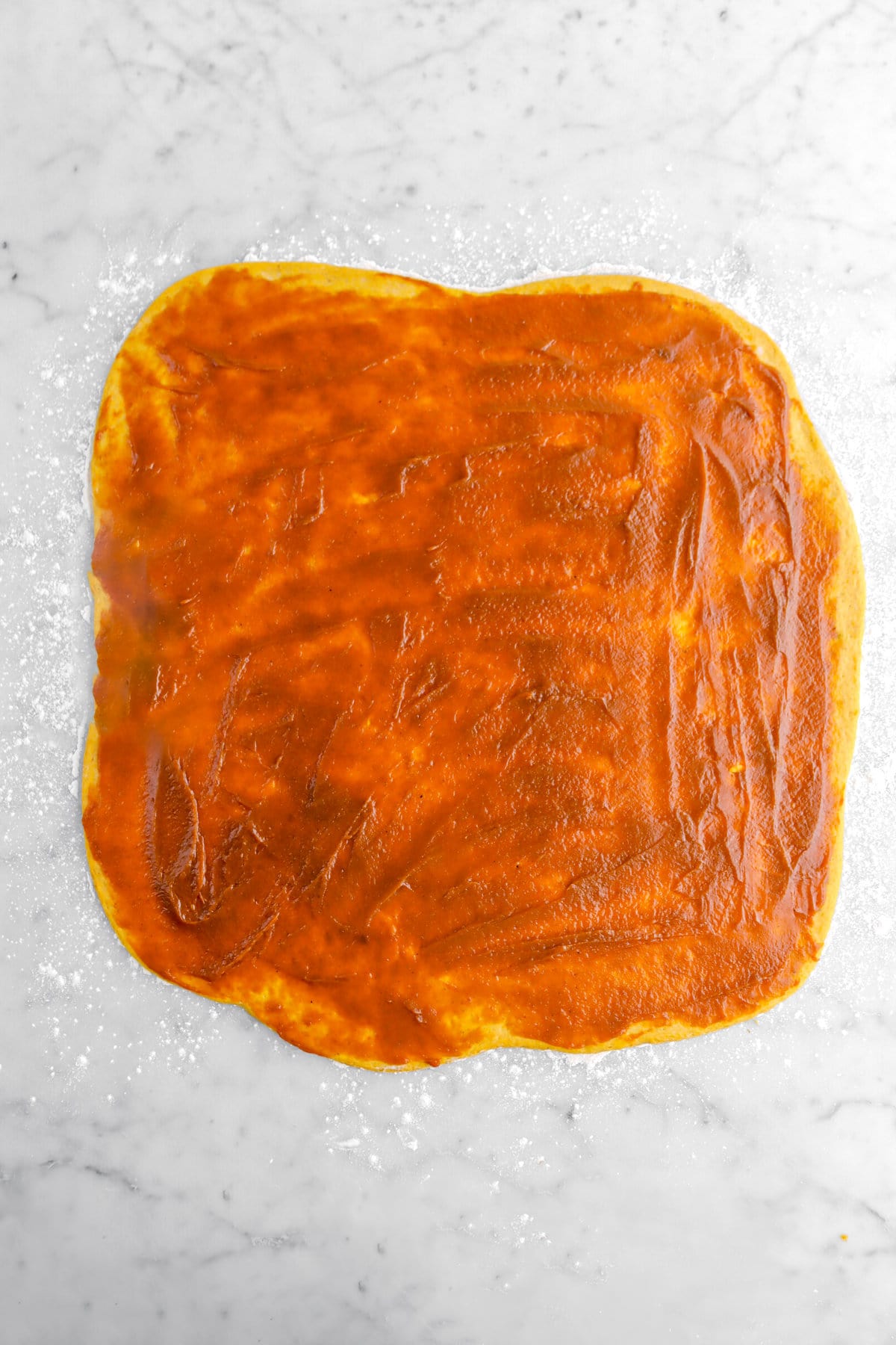 pumpkin butter spread across dough on marble surface.