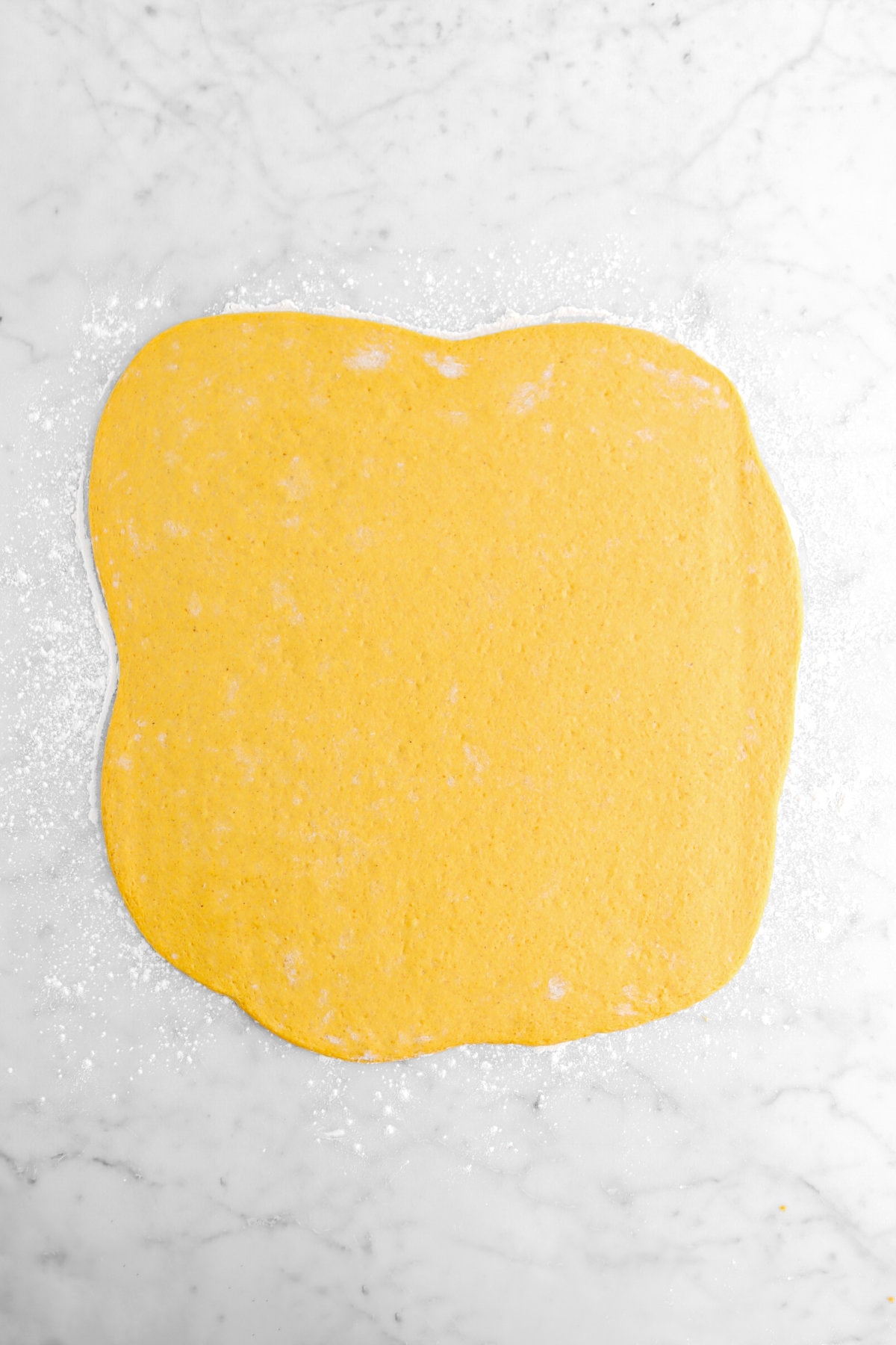 pumpkin dough rolled out into a square on marble surface.