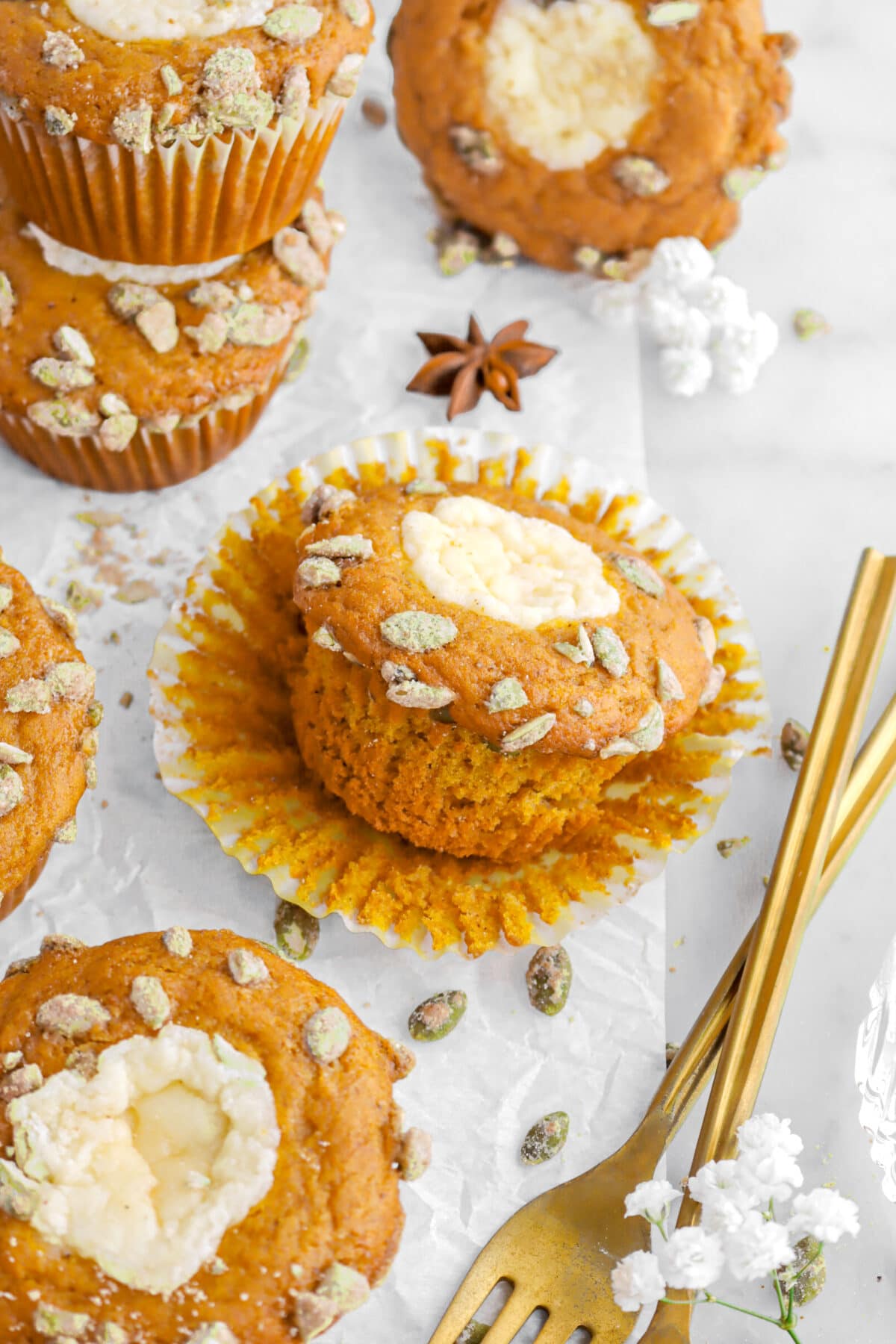 pumpkin muffin on top of cupcake paper with five muffins beside, two gold forks, and white flowers around.