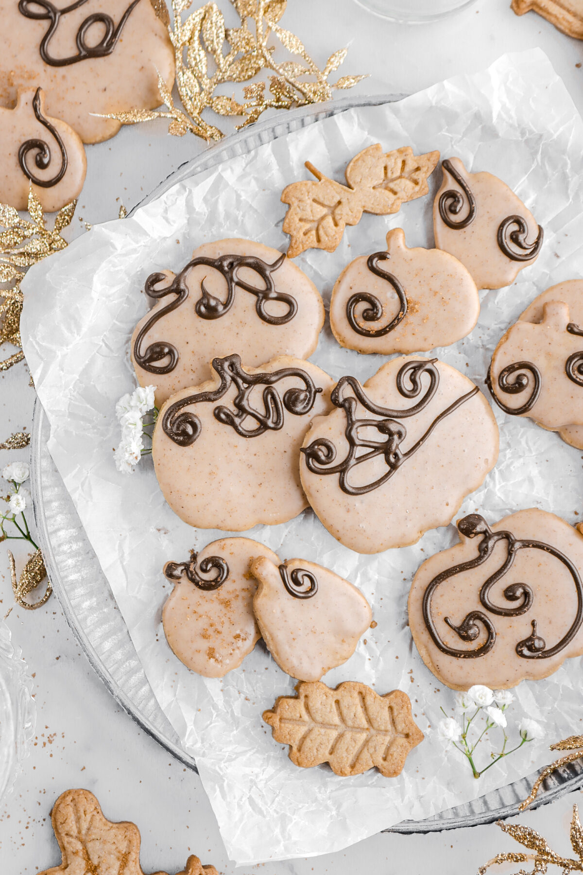 cropped overhead image of pumpkin shaped cookies on parchment paper won top of metal plate.